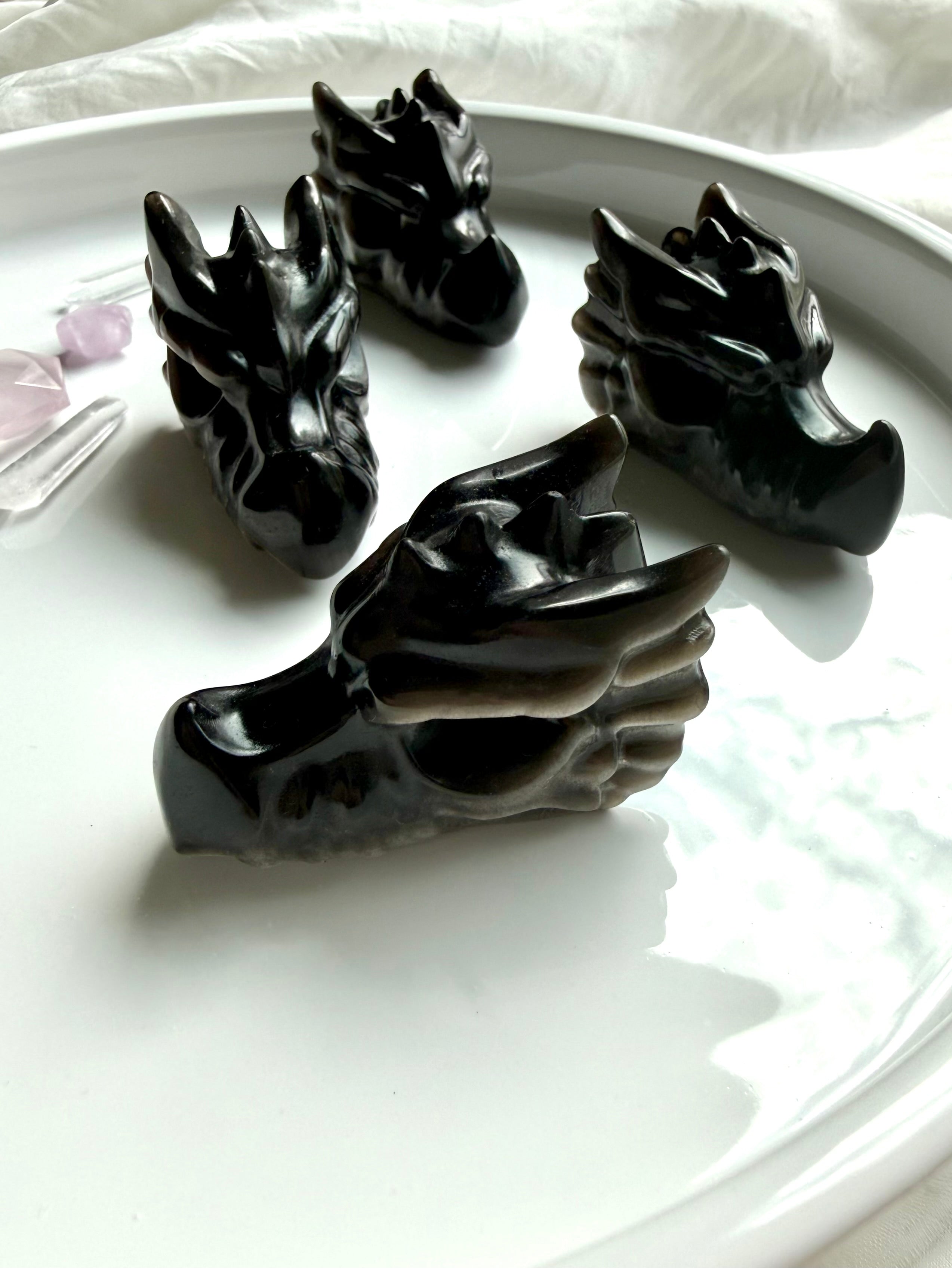 four silver sheen obsidian dragon carvings on neutral background, grounding crystals for protection and energetic clearing