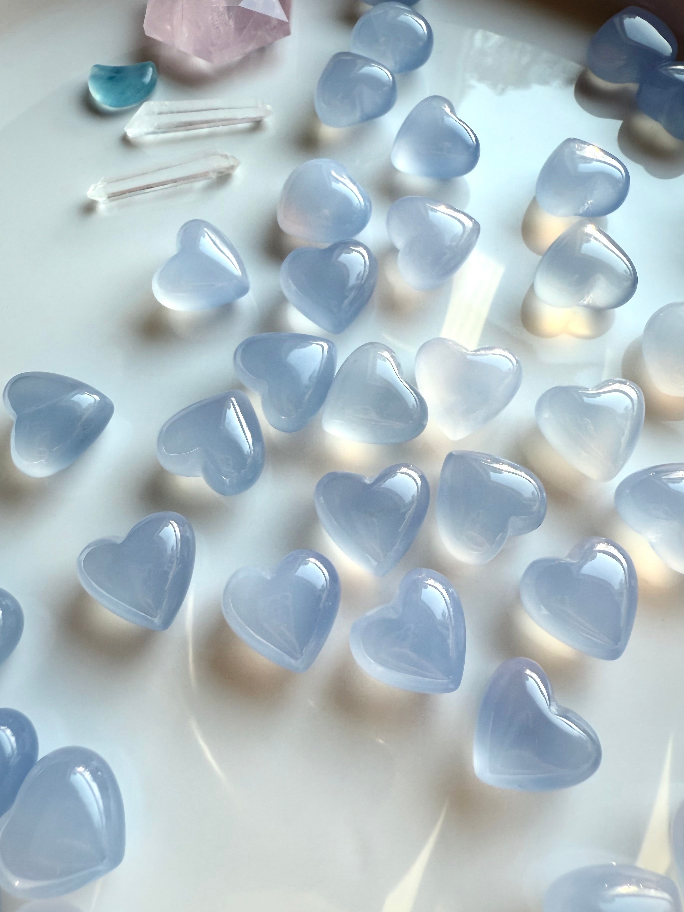 Mini Blue Chalcedony heart crystals scattered on a white tray with soft natural light, soothing blue crystal hearts for peaceful expression and clarity