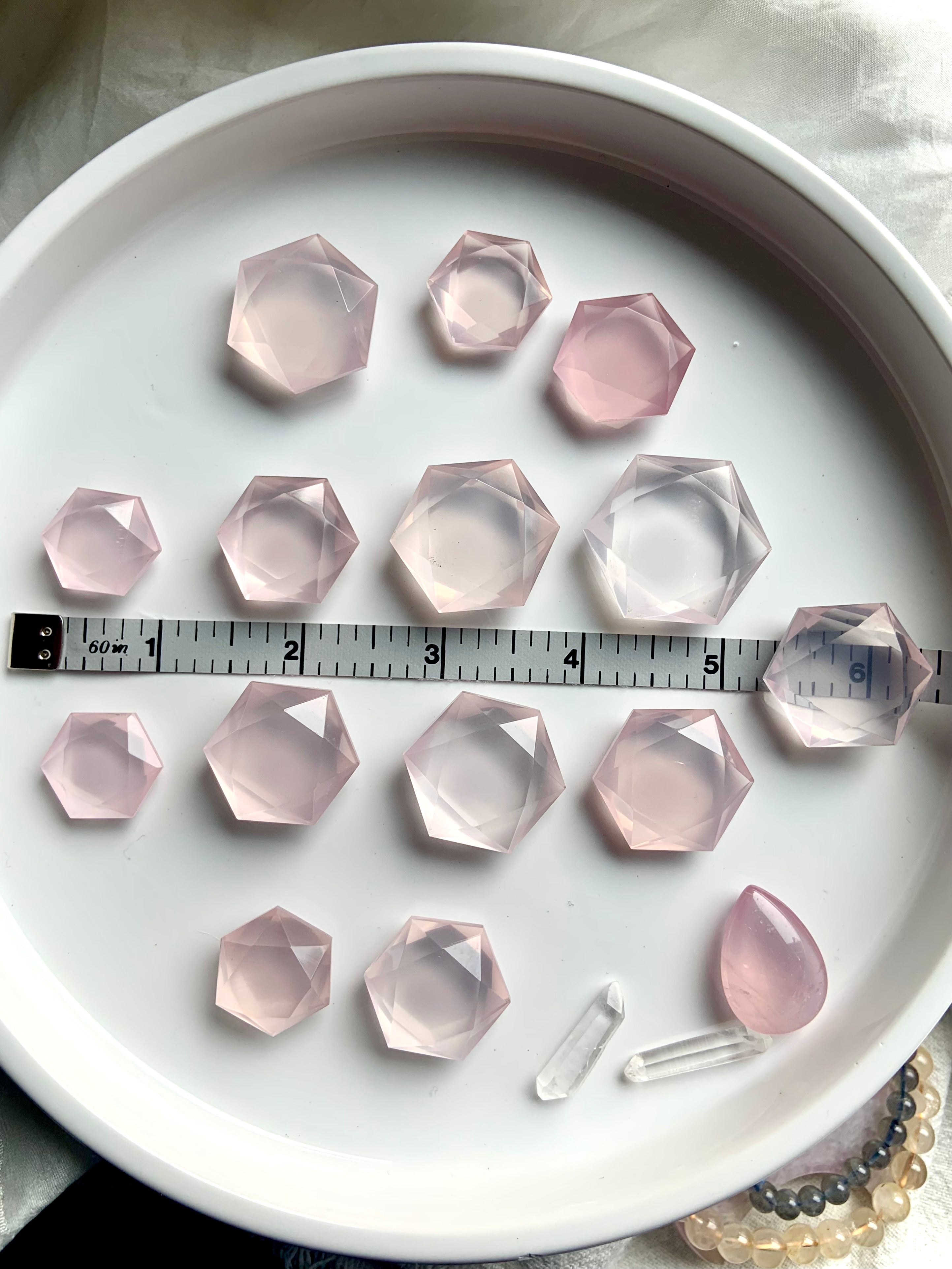 Faceted Rose Quartz hexagon crystals in mixed sizes shown with measuring tape, collector-grade sacred geometry stones for peace and love