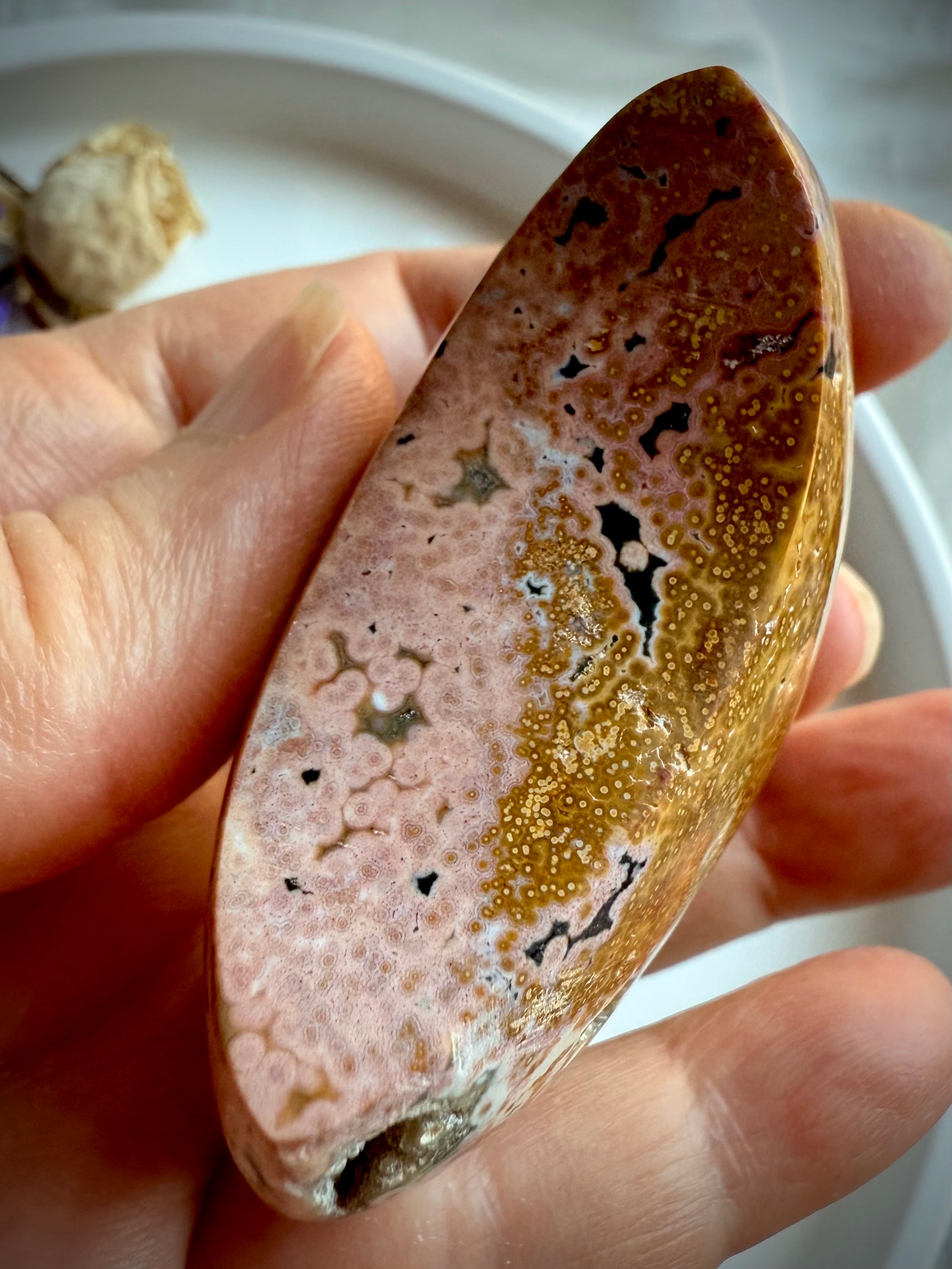 Side view of ocean Jasper moon crystal with peachy pink and golden yellow orbicular patterns held in hand for emotional healing