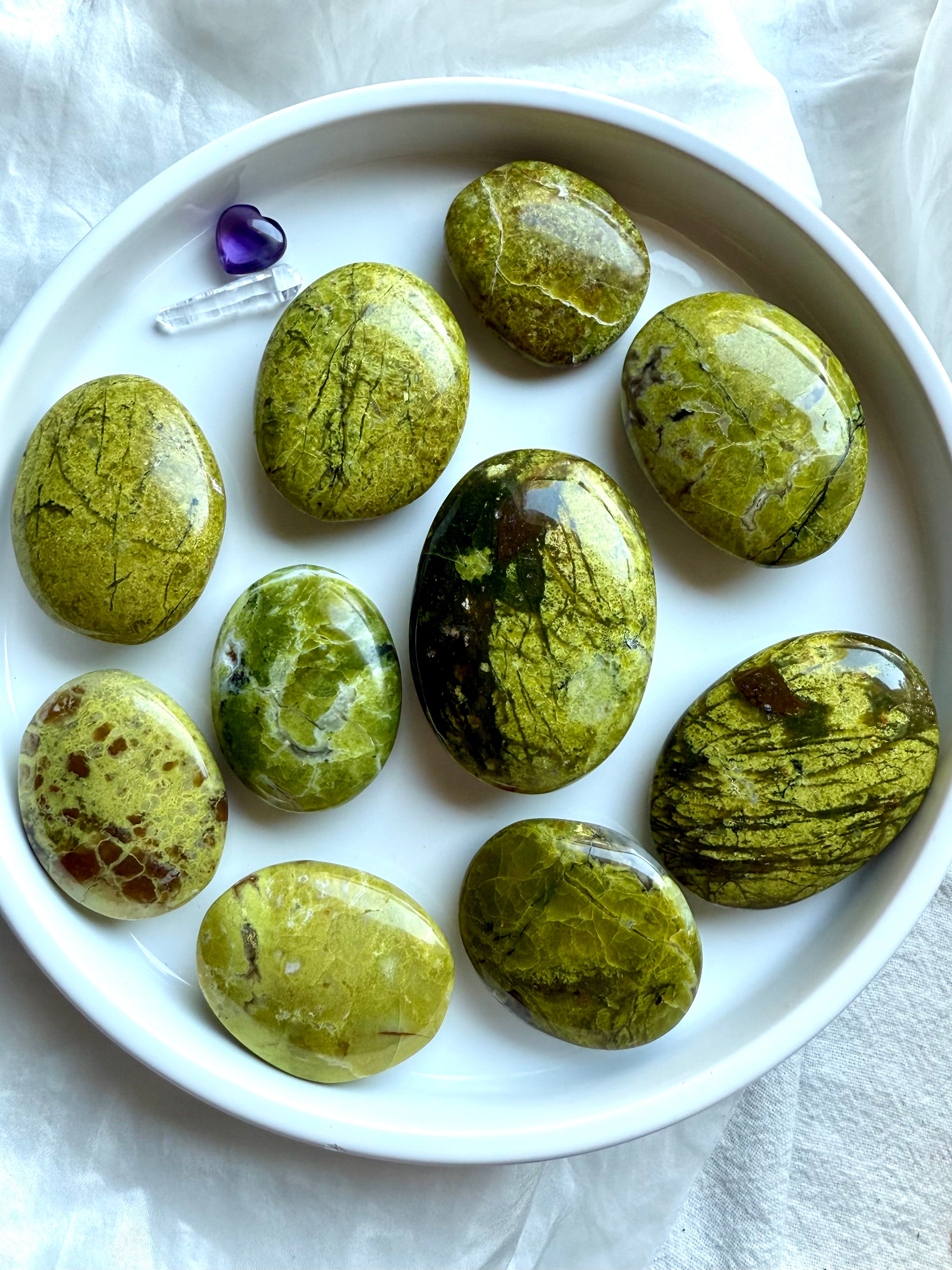 Arrangement of Green Opal palm stones on a white plate — luminous green crystals for heart chakra healing and emotional renewal.