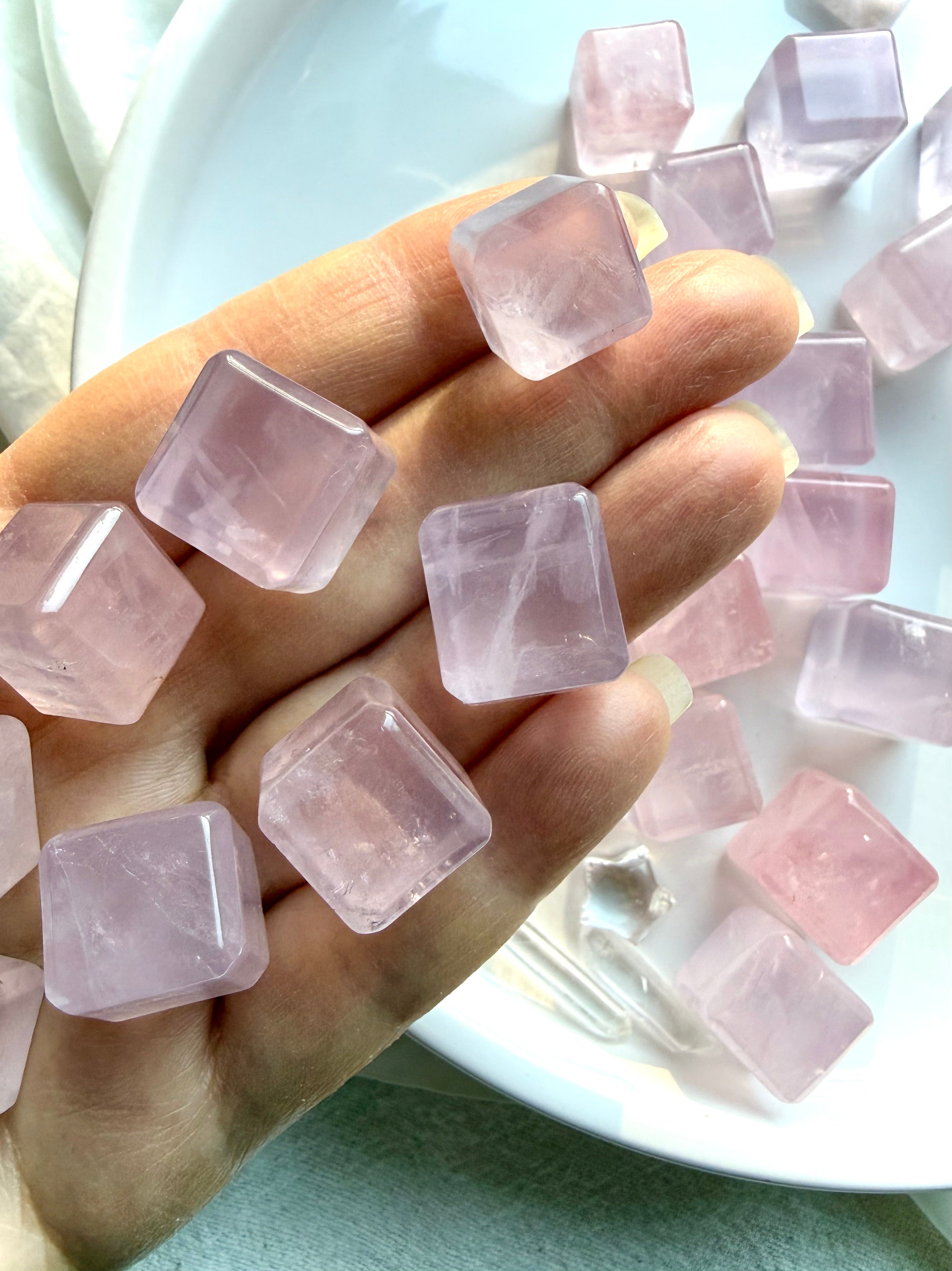 Rose quartz mini cube crystals held in hand with additional cubes in the background, polished heart chakra stones from Mozambique