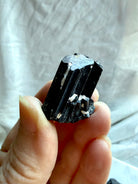 Raw Black Tourmaline chunk held in hand showing glossy columnar crystal growth and natural texture