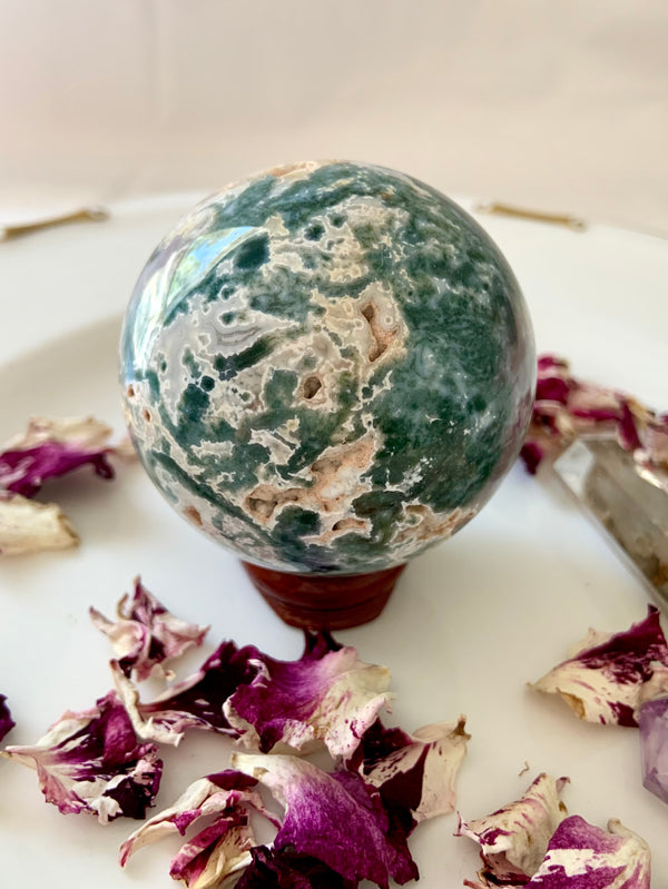 A beautiful blue green Druzy Moss Agate Crystal Sphere with white filigree patterns, comes with the wood stand in the pics. Shown on a creamy white background with rose petals.