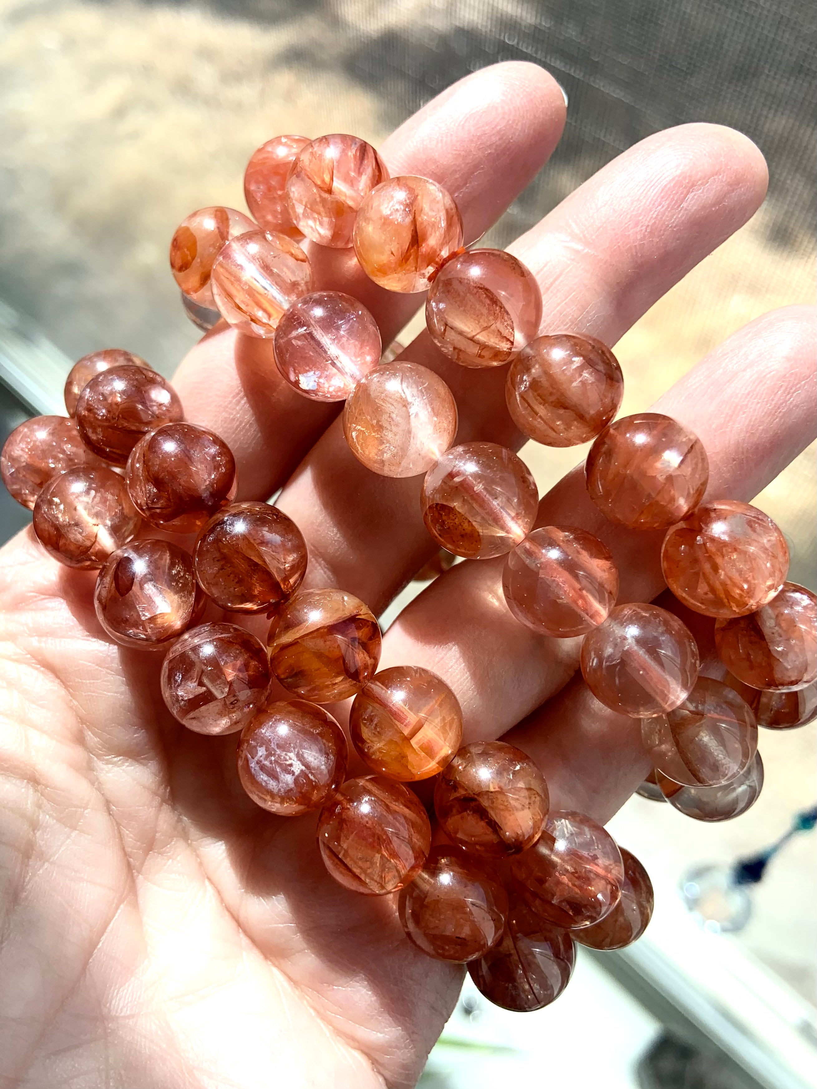 Four Fire Quartz bracelets held on hand, showing a mix of light and dark red quartz bead tones for variety in color and energy