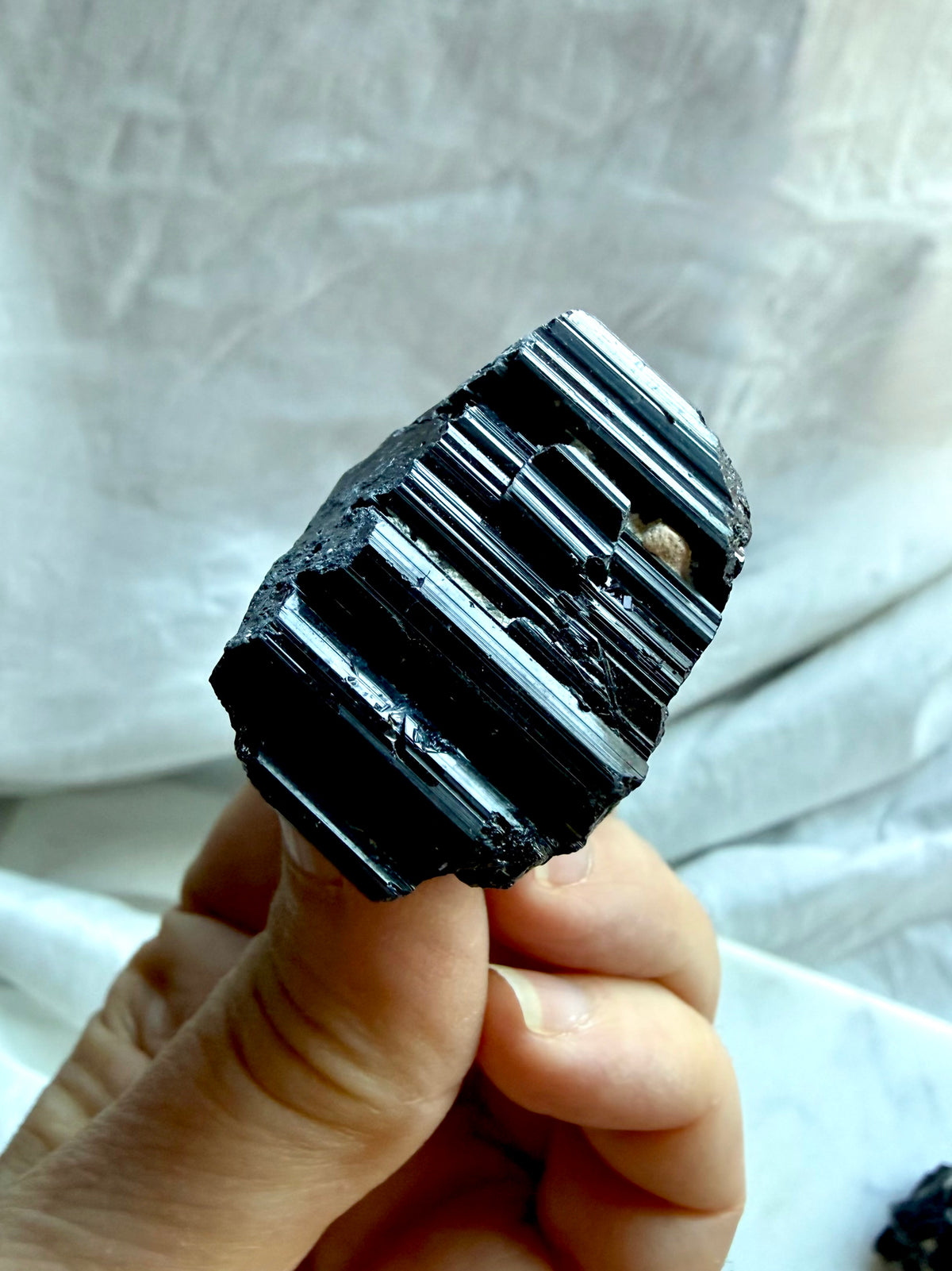 Raw Black Tourmaline crystal held in hand showing deeply grooved glossy black striations