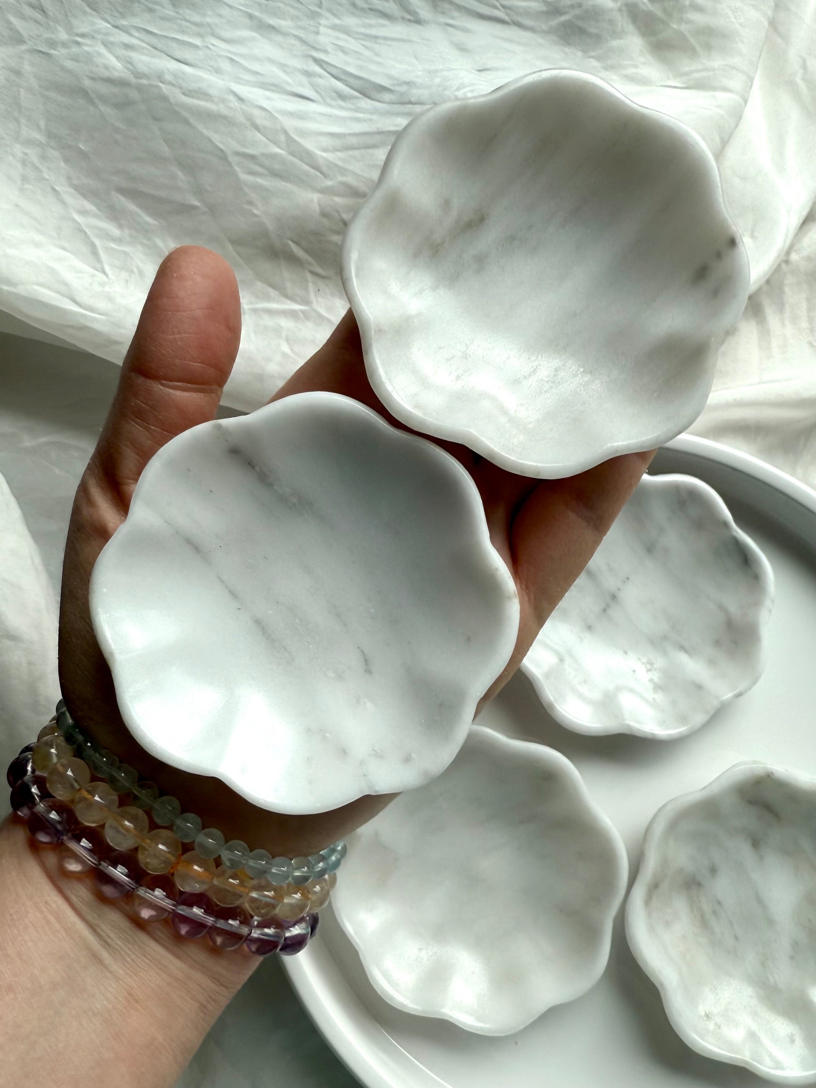 Two white marble daisy bowls shown in hand, with natural veining and smooth scalloped flower shape