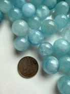 Mini Aquamarine sphere beside coin for scale – small blue March birthstone crystal ball