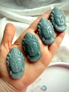 Blue Water Jade Quan Yin pendant carvings in hand showing natural color variation from sage to blueish green