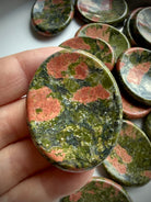 unakite worry stone held in hand showing green and pink mineral pattern for heart chakra healing