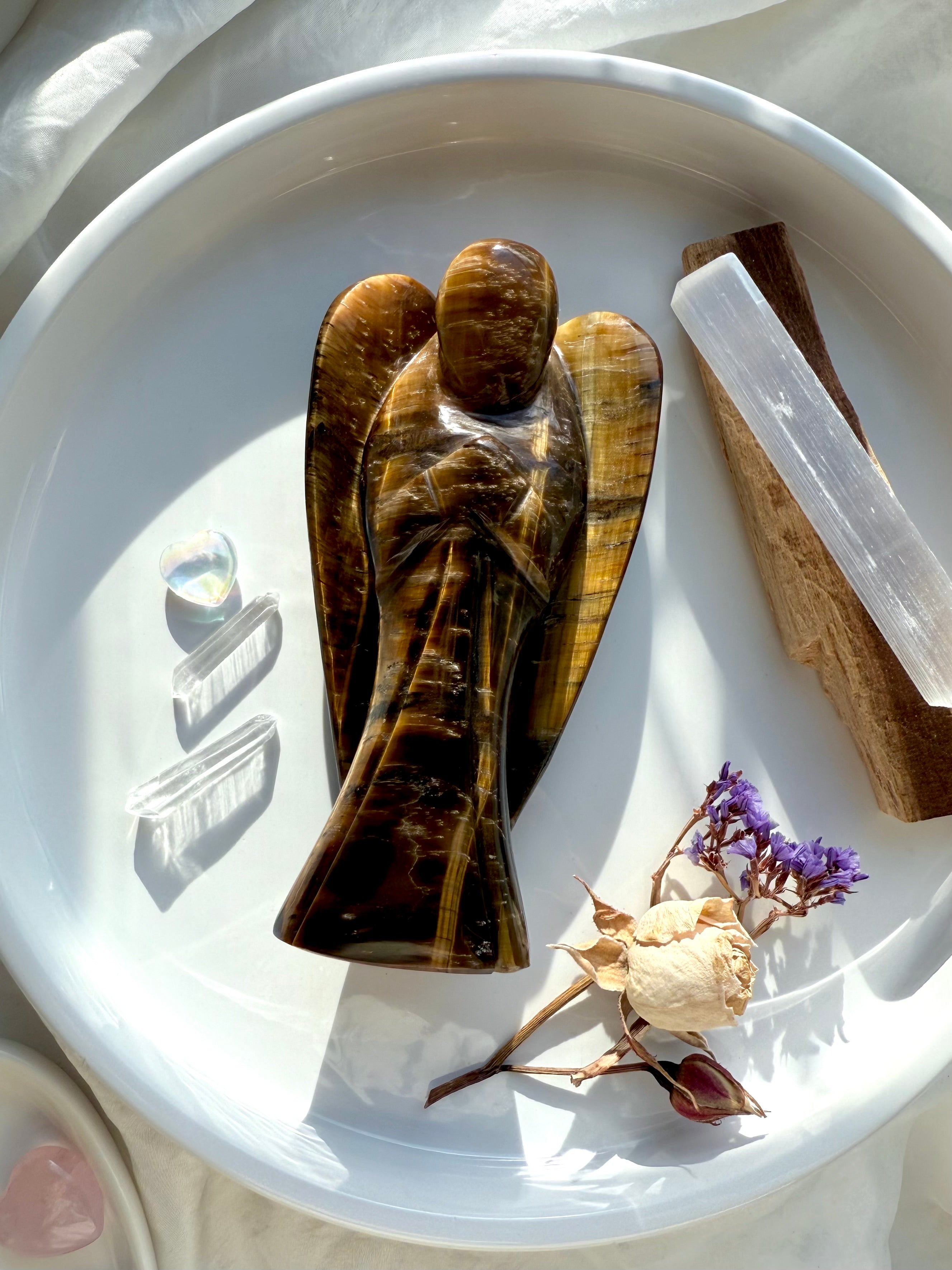 Golden Tiger’s Eye angel carving displayed in a white dish with Selenite, Palo Santo, and dried flowers