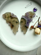 Carved agate butterfly wings with natural amethyst druzy on white tray, shown with quartz points and dried flowers.