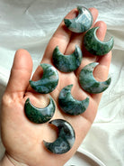 Array of Moss Agate crescent moon crystals in hand showing size and earthy green color.