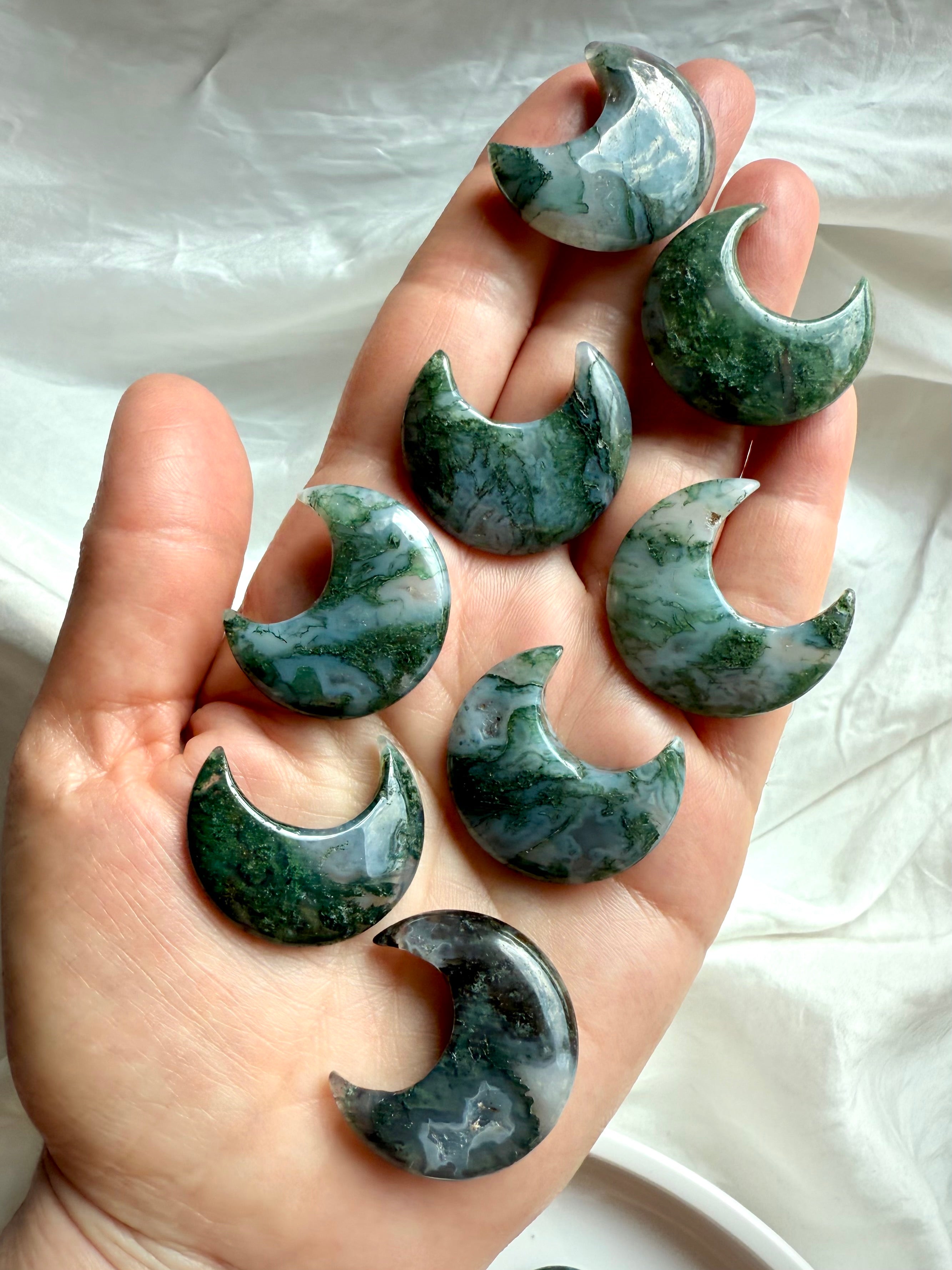Array of Moss Agate crescent moon crystals in hand showing size and earthy green color.