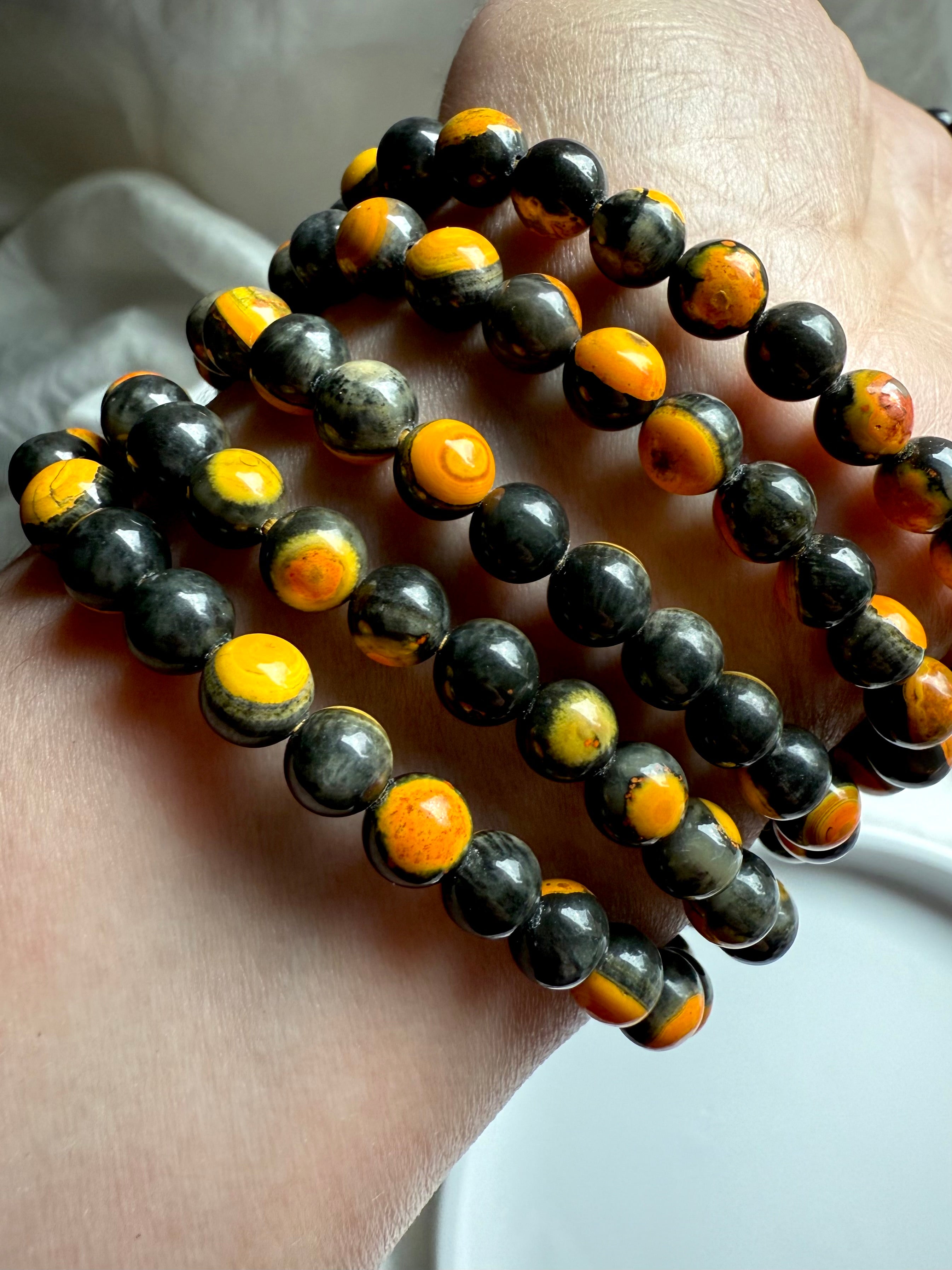 Five stacked bumblebee jasper bracelets laid out in a curved display, glowing yellow hues in radiant orbicular patterns