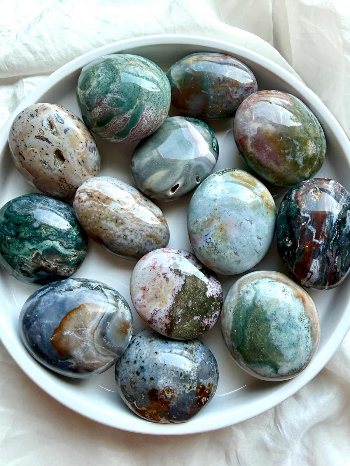 Ocean Jasper palm stones from Madagascar in a white bowl, showcasing teal, green, pink, cream, and gray colors with natural orbicular patterns