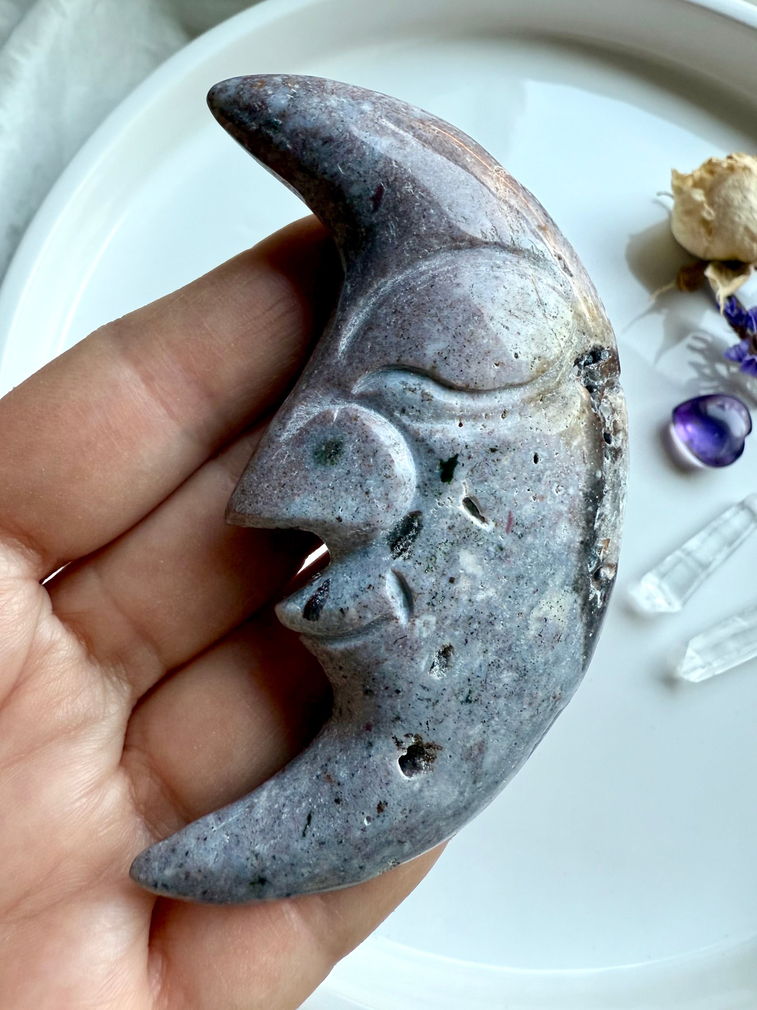 Ocean Jasper moon face carving in purple tones styled with flowers and healing crystals for decorative display.