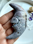 Ocean Jasper moon face carving in purple tones styled with flowers and healing crystals for decorative display.