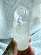 Brazilian Lemurian Quartz point held in hand with natural termination, ladder lines, internal veils, and inclusions