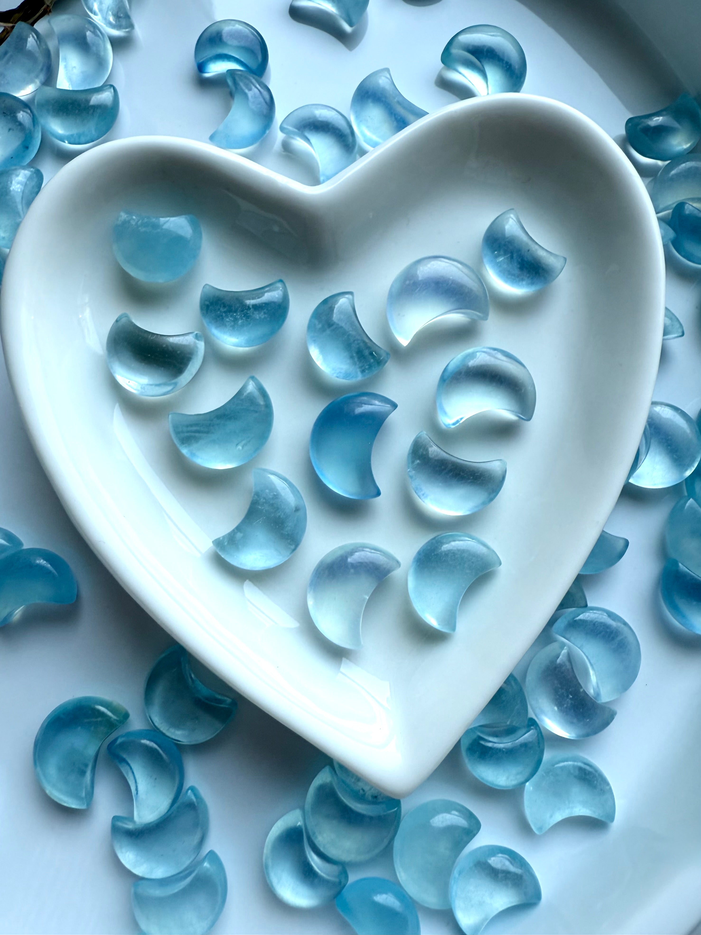 Closeup of Aquamarine moons inside a heart dish — deep ocean blue clarity and smooth polish captured in soft natural light