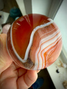 A banded carnelian crystal ball with an intricate chevron pattern swirling around the sphere