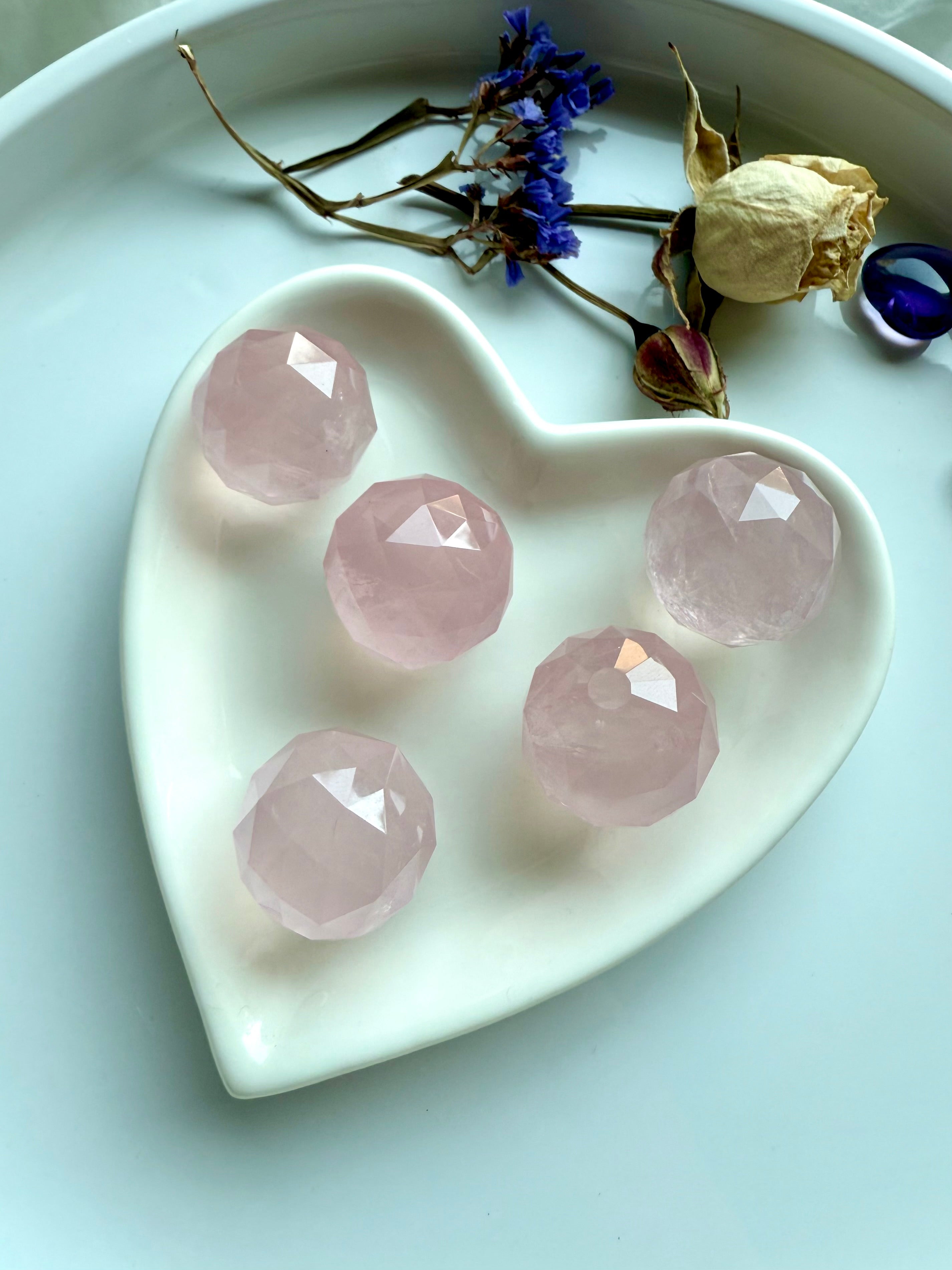 Faceted rose quartz crystal spheres inside a heart-shaped white dish. Soothing pink crystals for love.