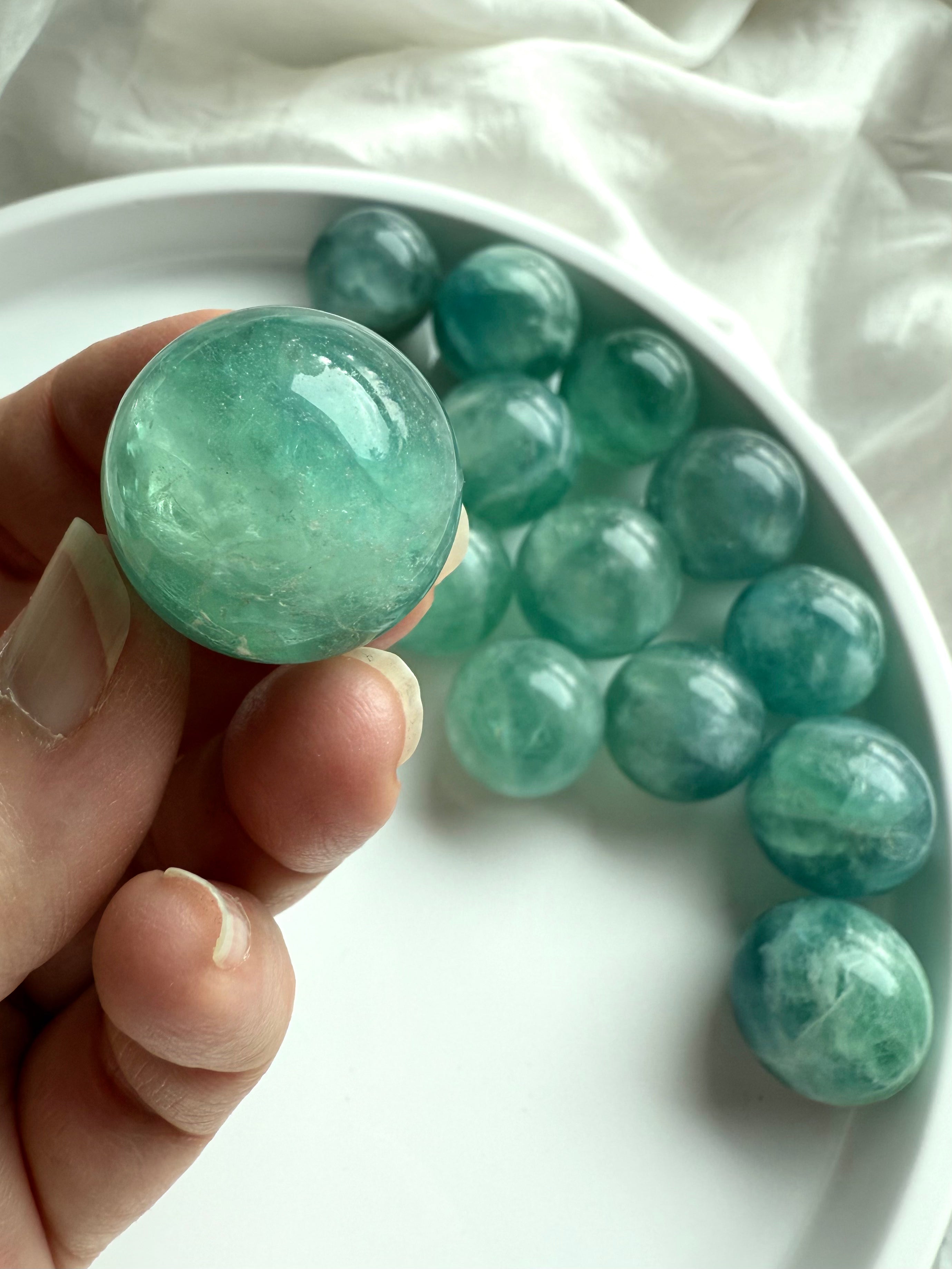 Hand holding a mini teal Fluorite sphere with shimmering aqua tones for clarity, calm, and focus. 