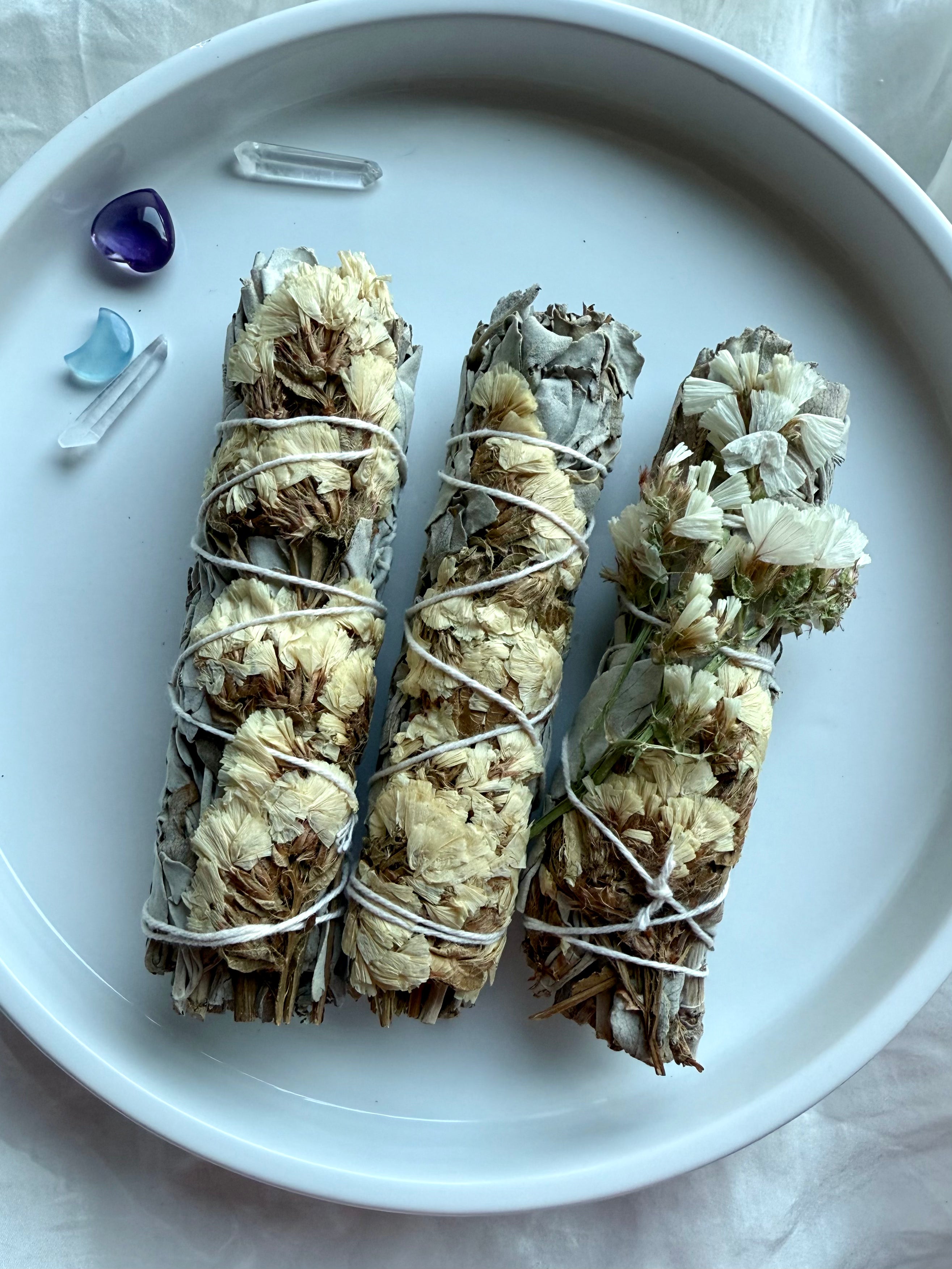 White sage smudge bundles wrapped with natural white statice flowers on white plate for energy clearing and spiritual rituals