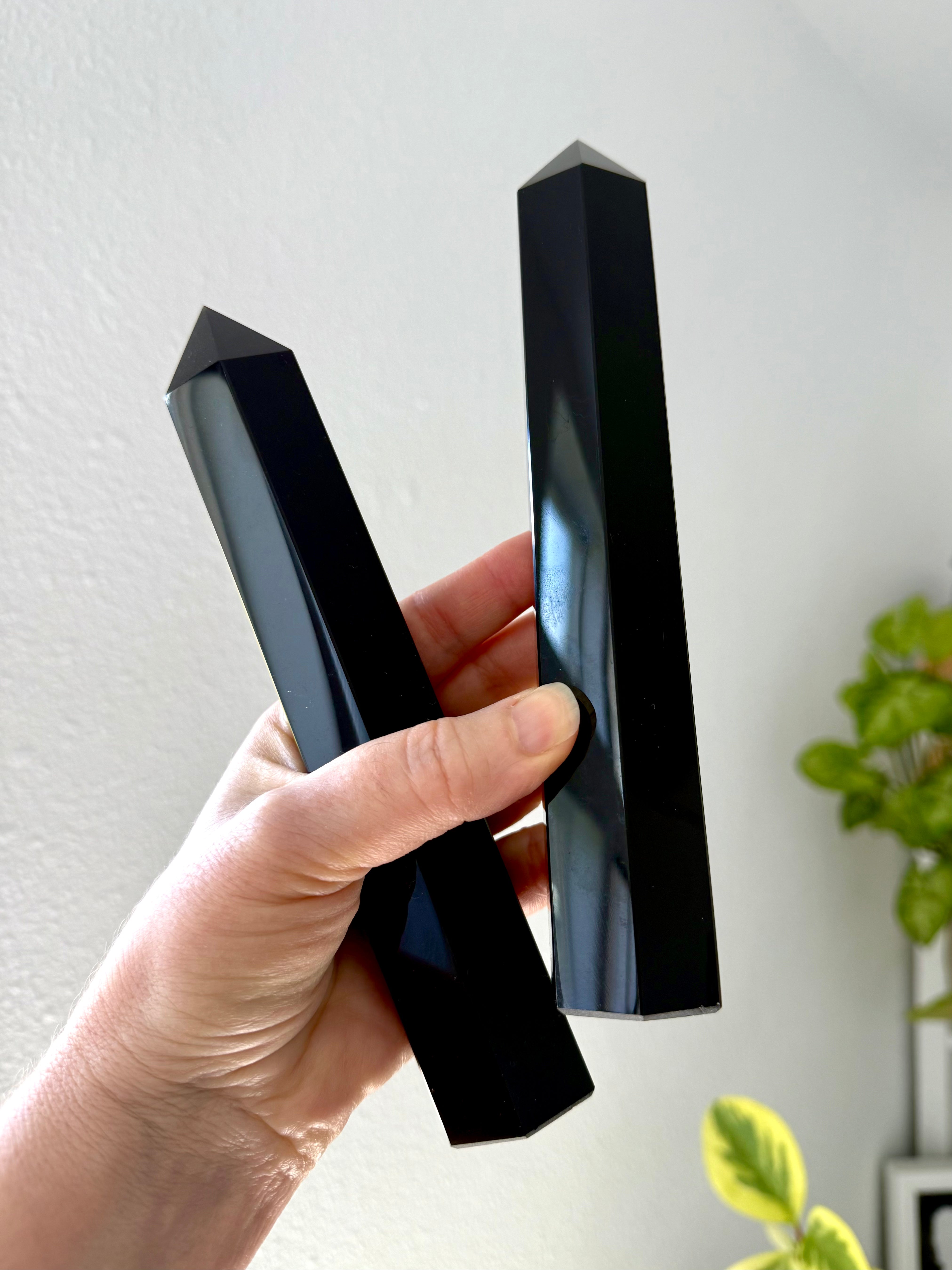 Hand holding two large Black Obsidian towers at an angle — glossy polished crystals for energetic protection & grounding.