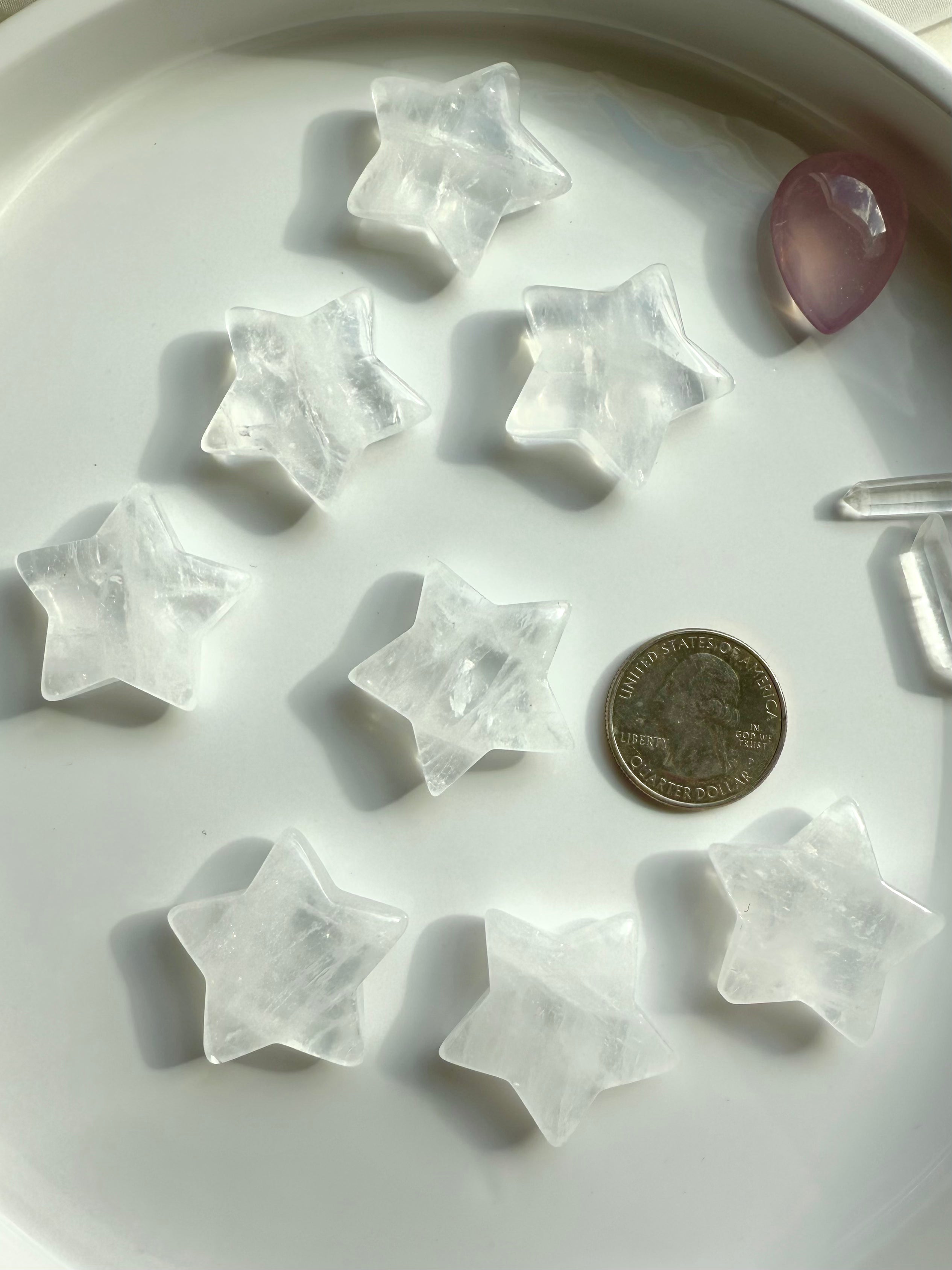 Clear Quartz star carvings on white plate with quarter for size reference, small healing crystals for chakra balancing and grids