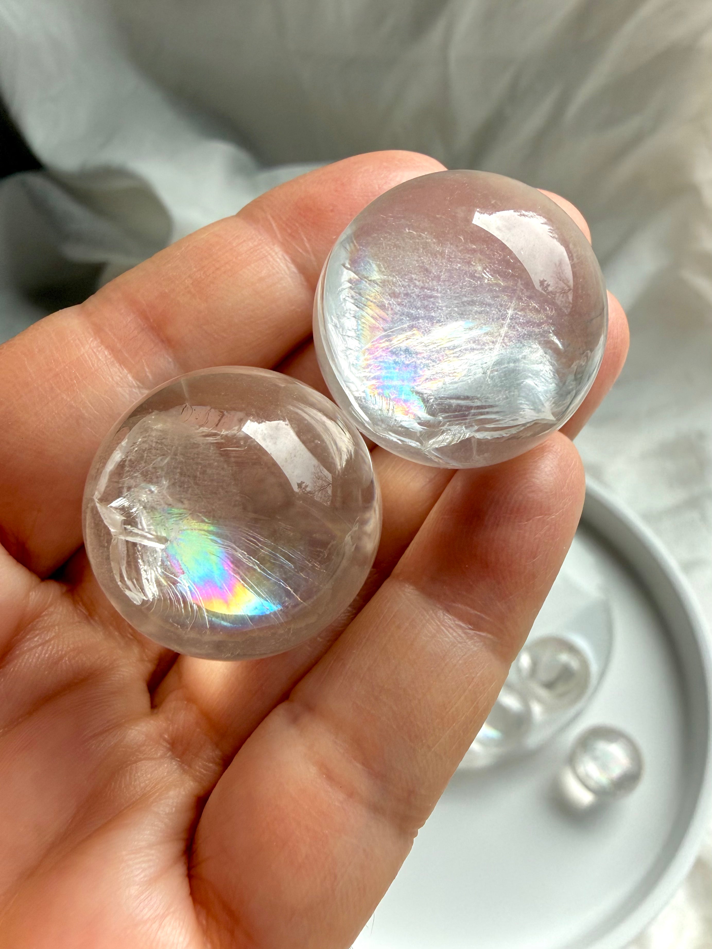 Hand holding two rainbow girasol mini quartz spheres, milky crystal ball with soft ethereal glow and natural rainbow inclusions