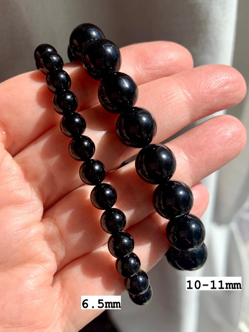 Two Black Tourmaline bracelets on hand marked 6.5mm and 10–11mm bead sizes — ideal for showcasing sizing and crystal bead quality