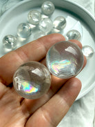 Close-up of two rainbow girasol mini quartz spheres in hand, milky crystal balls with luminous opaline glow and subtle silvery rainbows