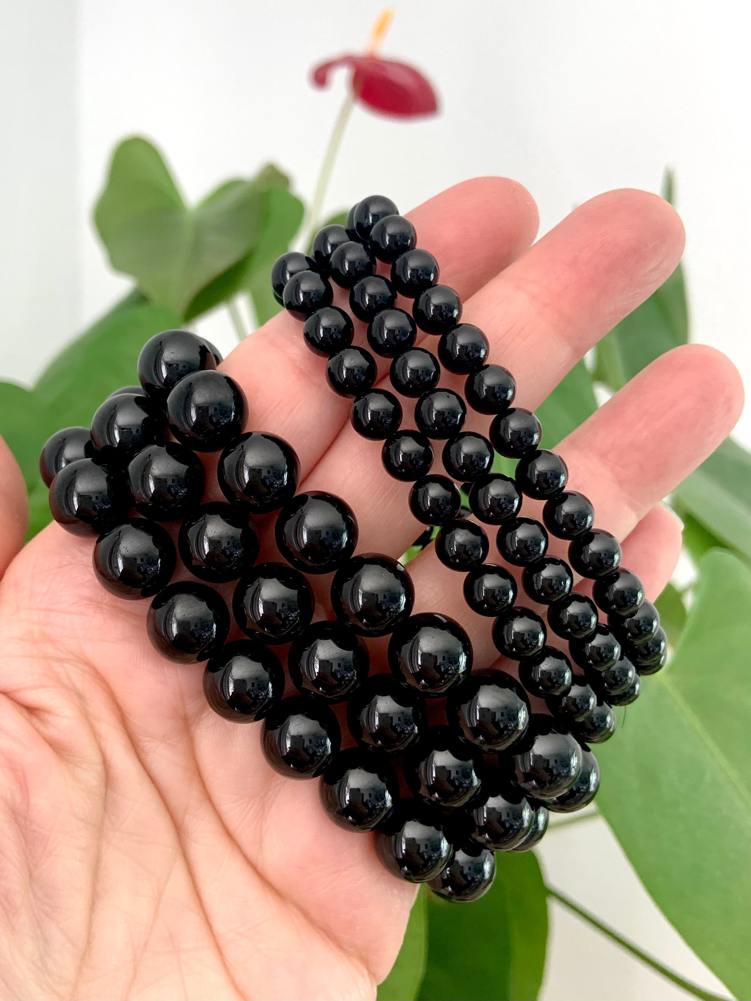 Side view of two sets of Black Tourmaline bracelets on a hand — showing glossy bead sizes 10–11mm and 6–7mm for sizing reference