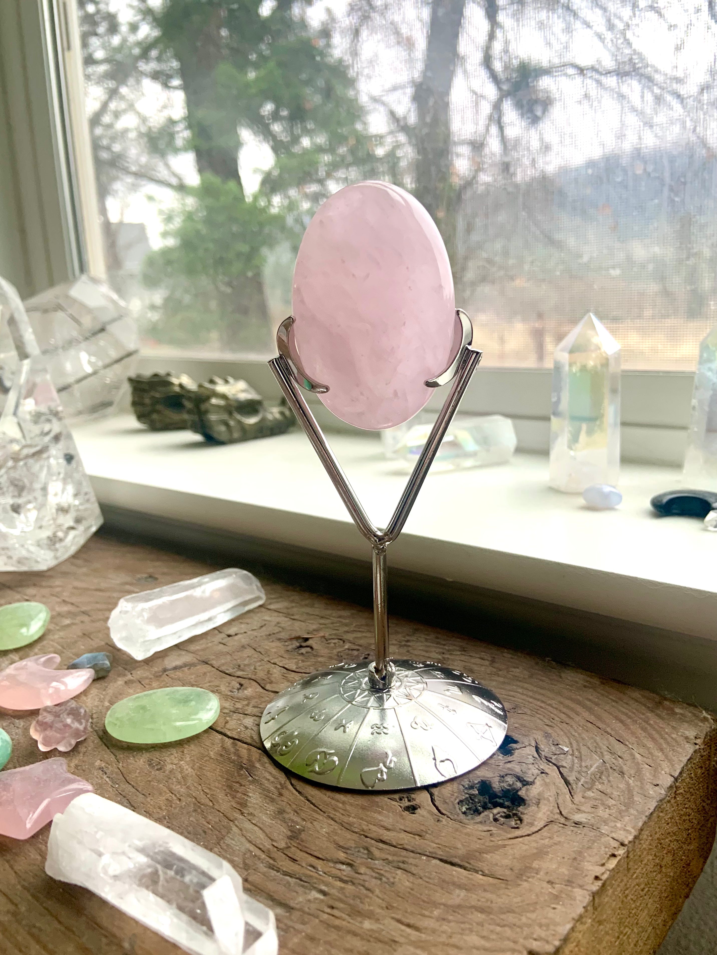 Silver crystal holder with Rose Quartz palm stone — shown in a windowsill with other crystals, ideal for serene crystal decor and display.