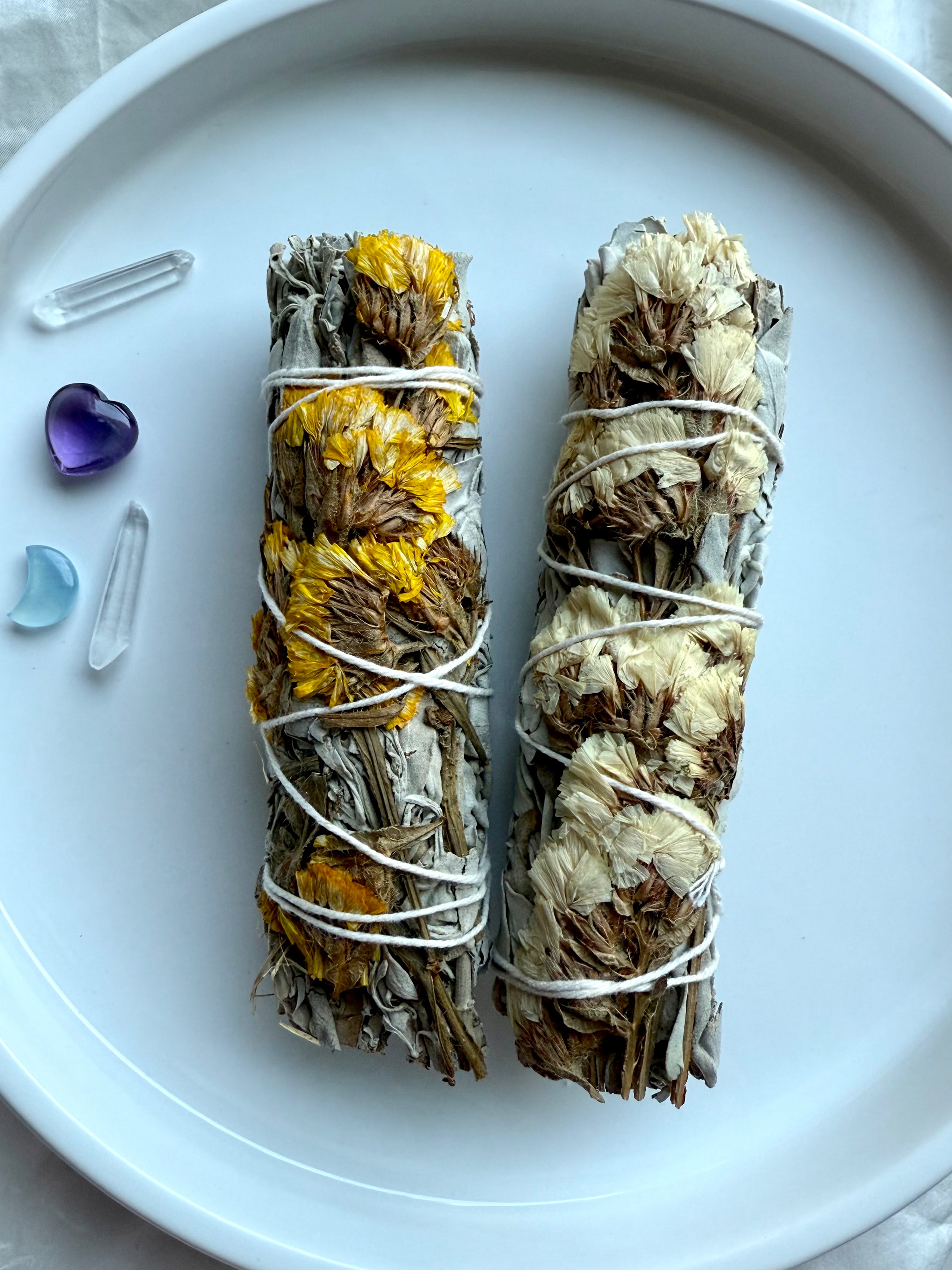 White sage smudge bundles wrapped with yellow and white statice flowers, styled with amethyst, aquamarine, and quartz crystals for energy clearing, spiritual cleansing, and crystal rituals.