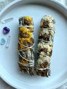 White sage smudge bundles wrapped with yellow and white statice flowers, styled with amethyst, aquamarine, and quartz crystals for energy clearing, spiritual cleansing, and crystal rituals.