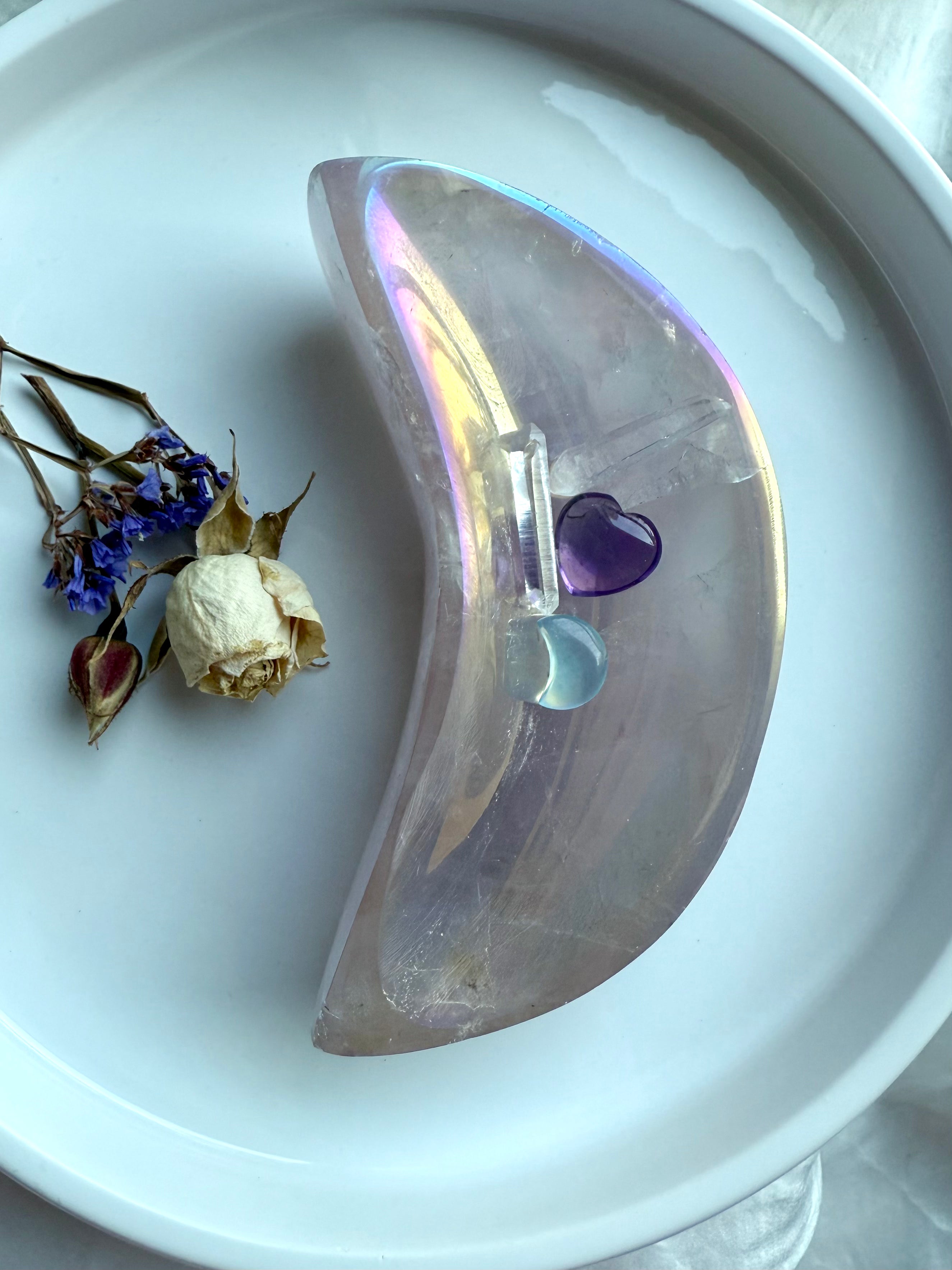 Aura Rose Quartz crescent moon bowl with opalescent lilac shimmer, displayed with dried flowers, mini hearts, and clear quartz points