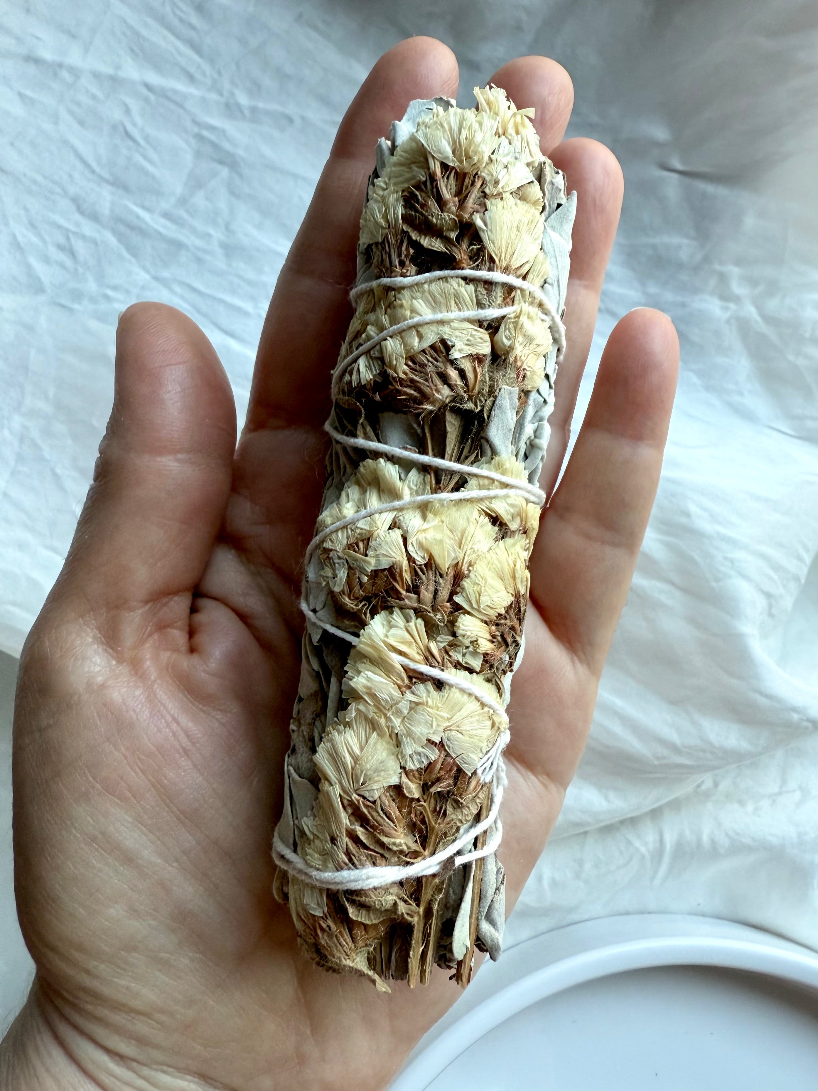 Single white sage smudge stick with white statice flower shown in hand for scale and size reference