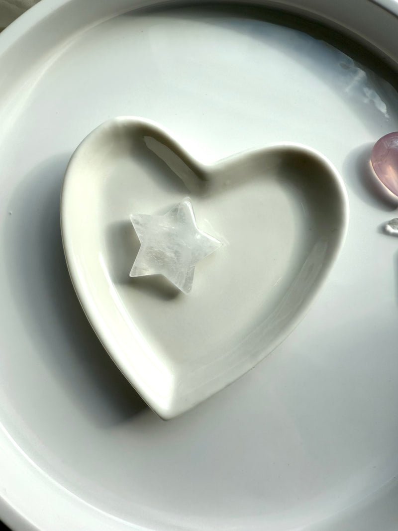 One clear quartz star shown on a white ceramic heart bowl