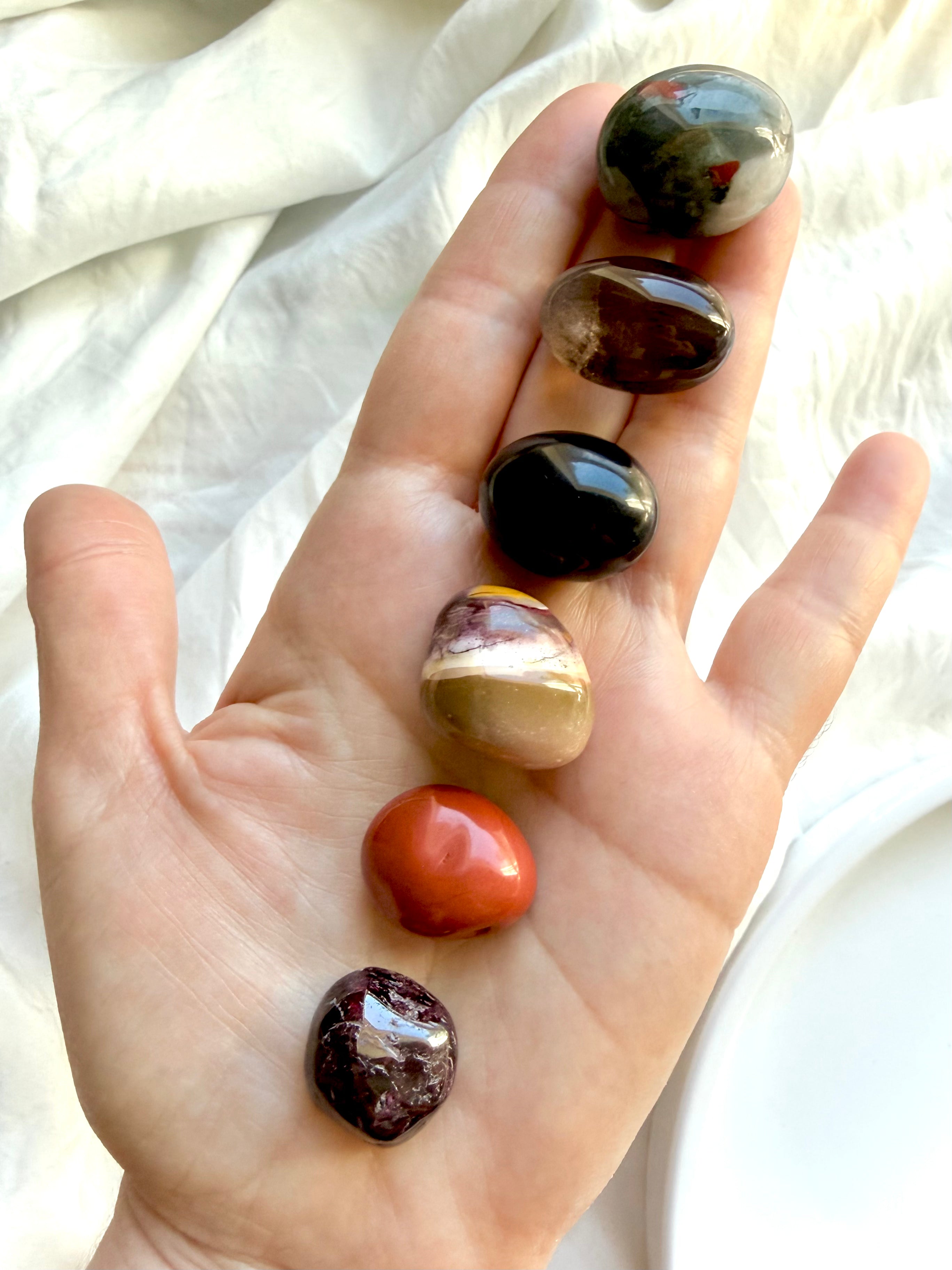 Hand holding a Root Chakra Crystal Set with Bloodstone, Black Obsidian, Red Jasper, Smoky Quartz, Garnet, and Mookaite Jasper