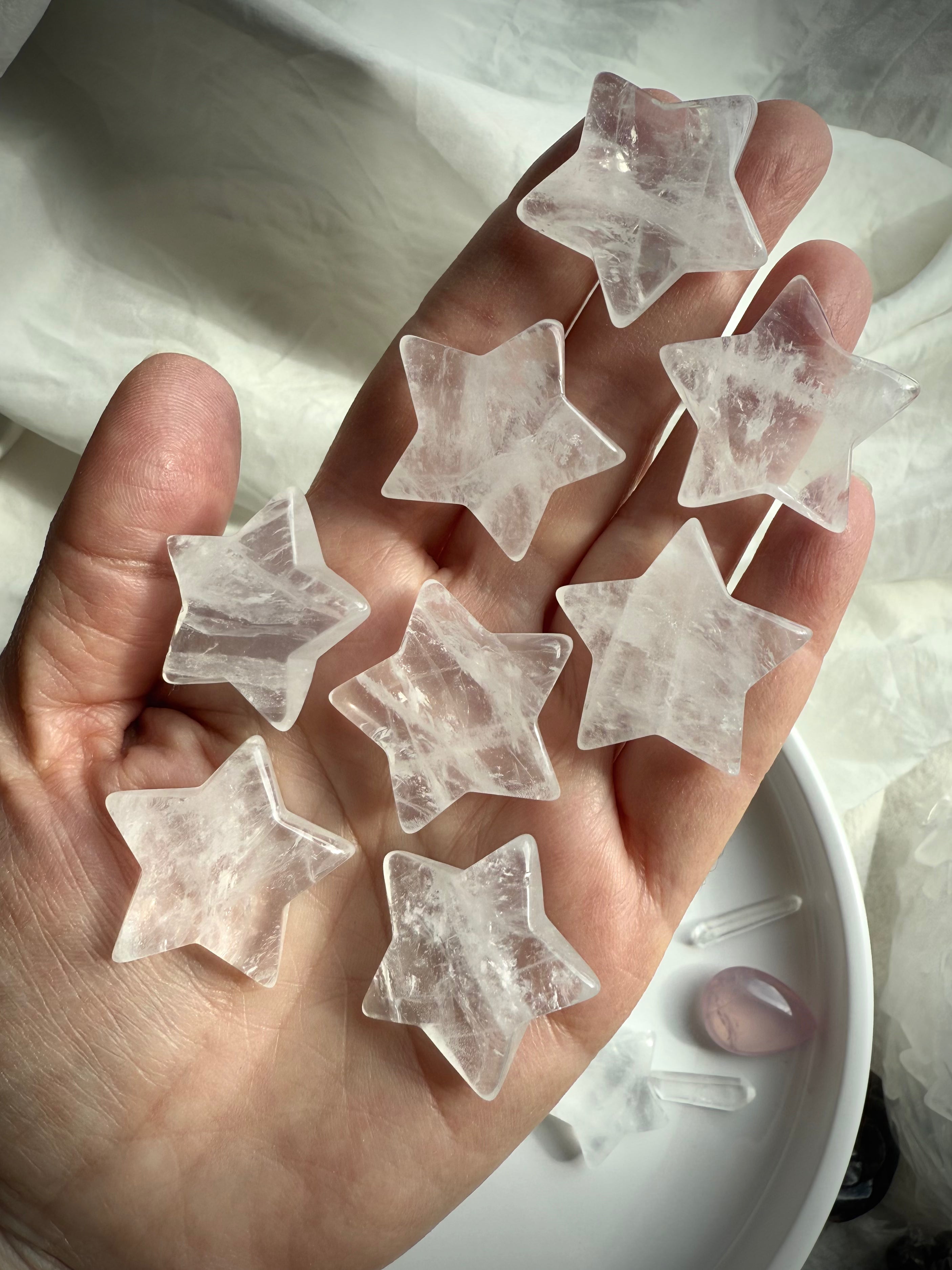 Clear Quartz stars displayed on hand over white silk, luminous crystal carvings for clarity and chakra healing