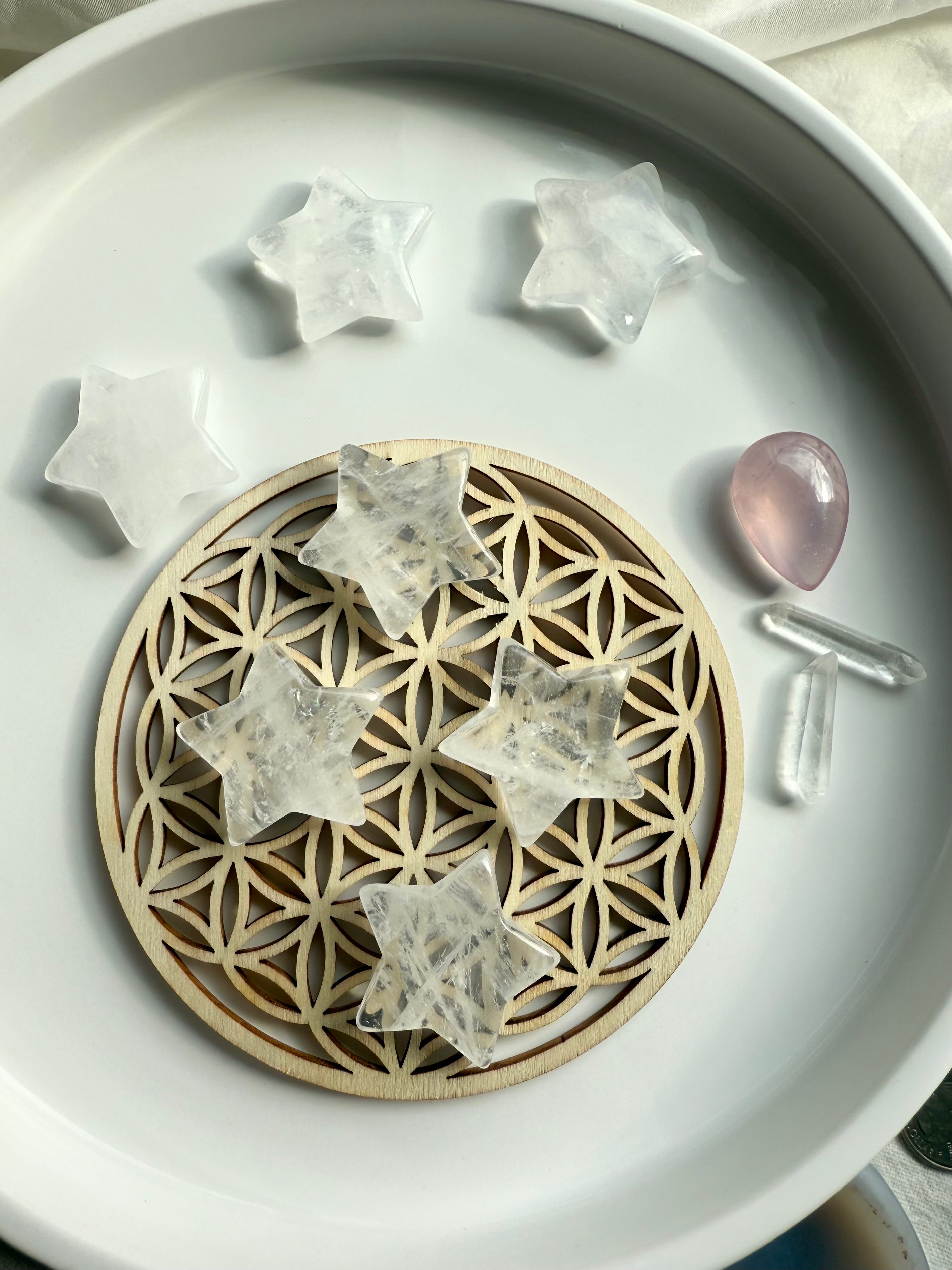 Clear Quartz stars shown on wooden Flower of Life grid placed on a white plate with other crystals, sacred geometry altar décor