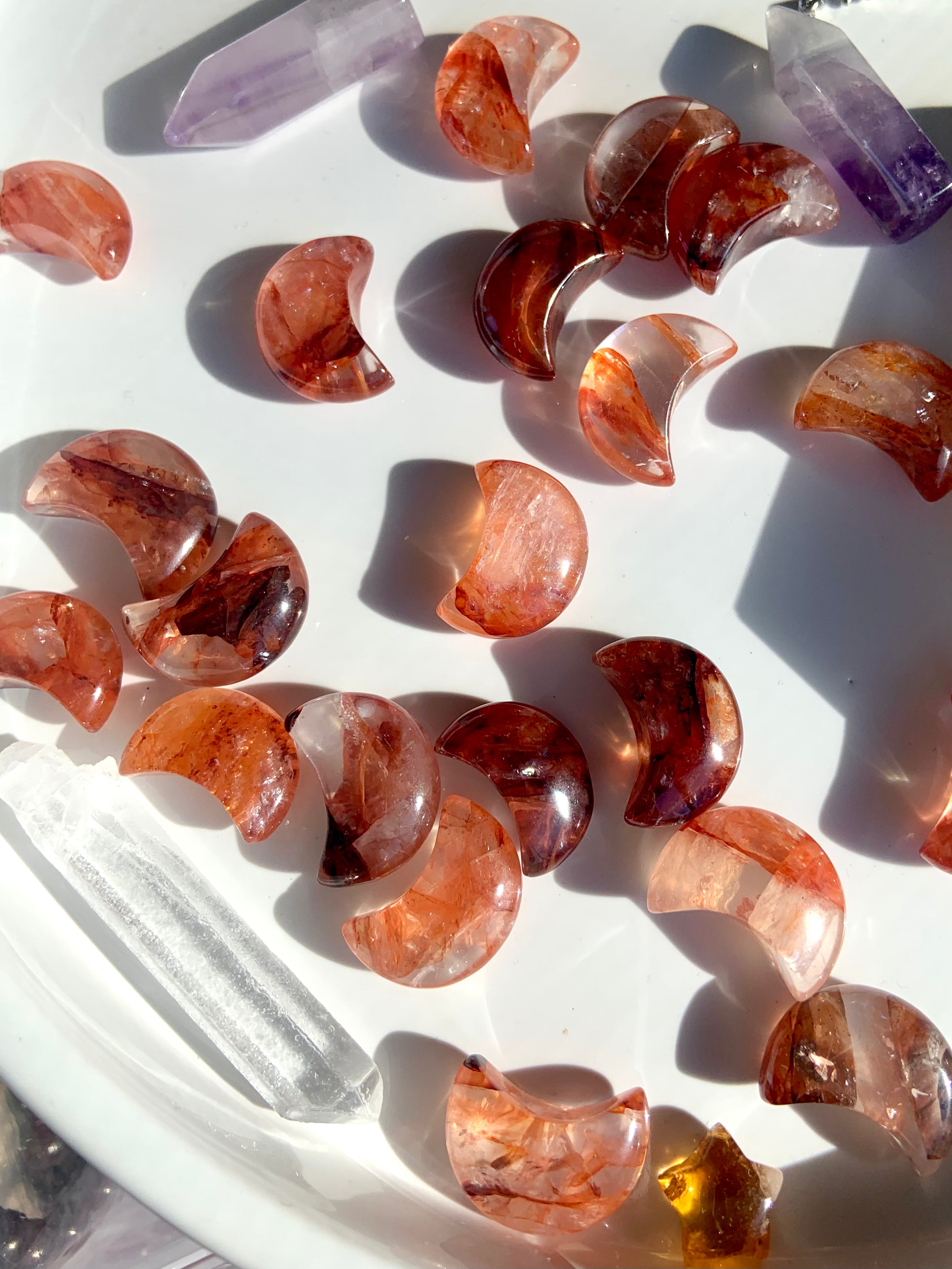 An array of vibrantly colored mini sized fire quartz crescent moons on a white plate with some other crystals