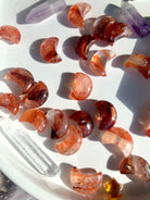 An array of vibrantly colored mini sized fire quartz crescent moons on a white plate with some other crystals