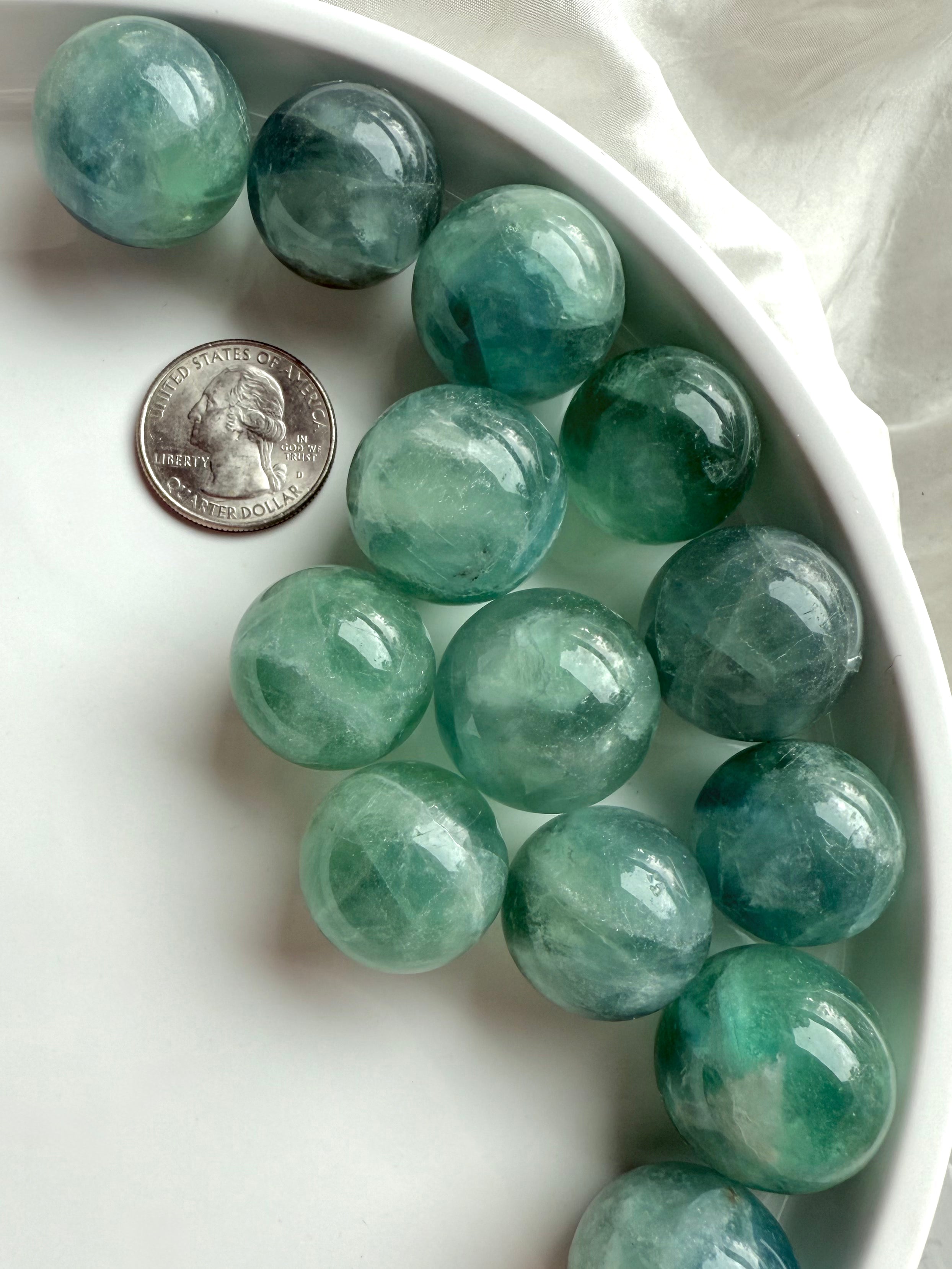 Mini teal Fluorite crystal spheres with aqua tones next to a U.S. quarter for size comparison.