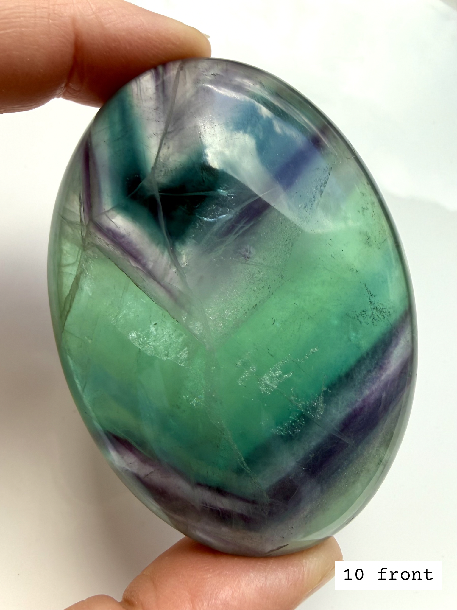Teal fluorite palm stone 10 front held to the light, highlighting vivid blue green striping and clarity