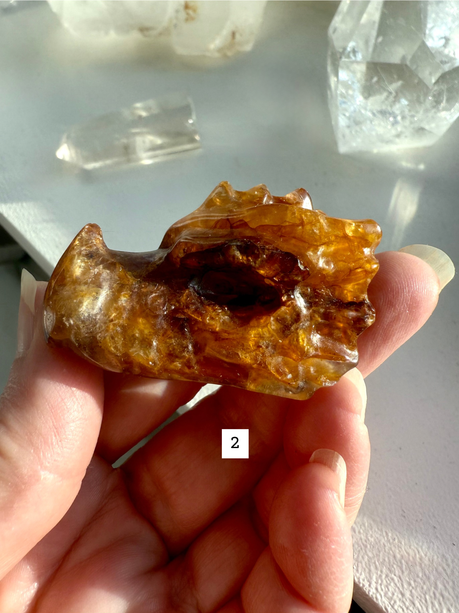 Hand holding Golden Healer Quartz dragon head with hematite inclusions and golden light patterns — crystal carving for chakra alignment and energy healing.