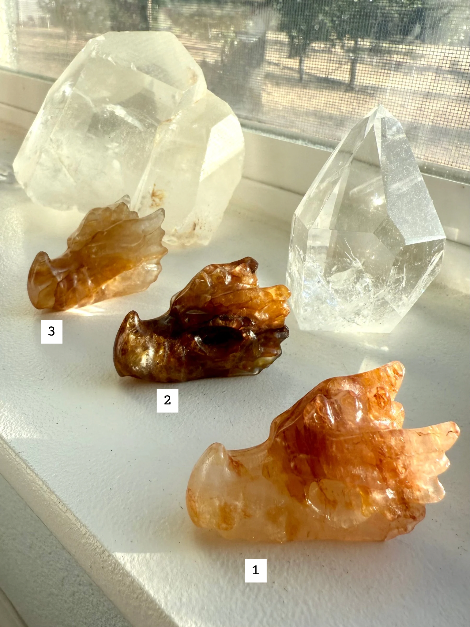 Numbered Golden Healer Quartz dragon head carvings displayed on windowsill — crystal dragon figurines with golden hematite inclusions for chakra healing and spiritual gifting.