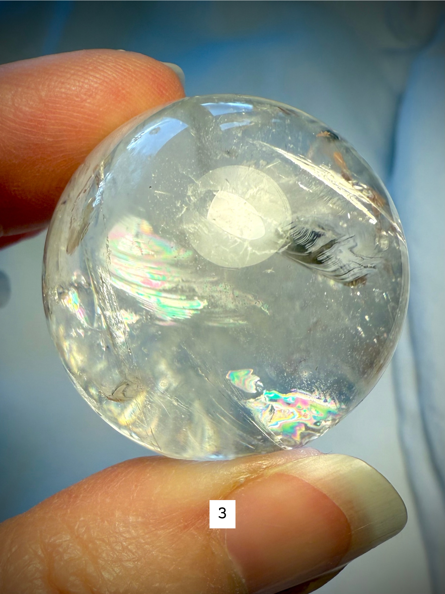 Hand holding Rainbow Quartz sphere #3, highlighting brilliant internal rainbows and natural inclusions.